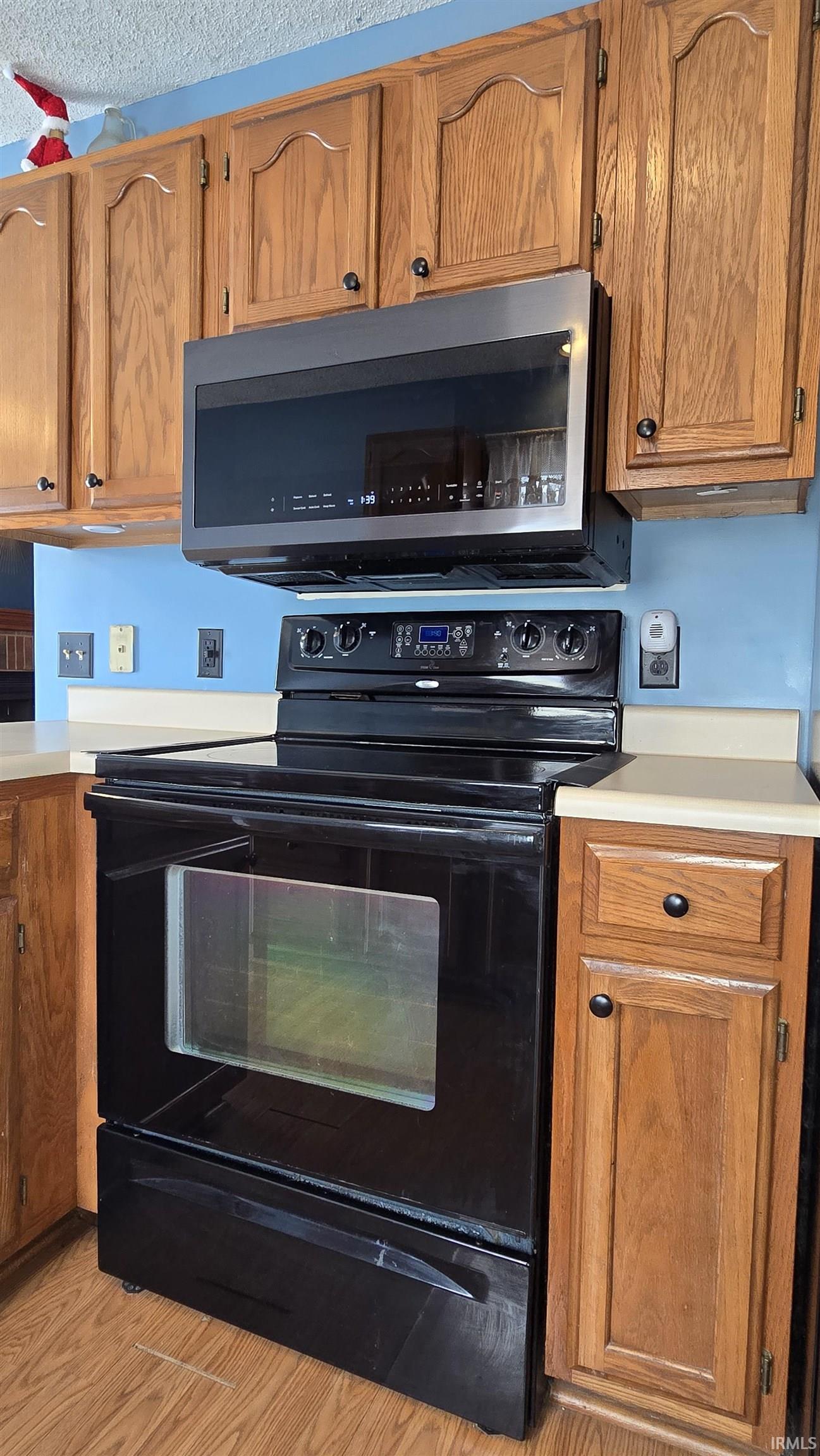 Kitchen featuring black / electric stove, light countertops, brown cabinets, stainless steel microwave, and light wood-style floors