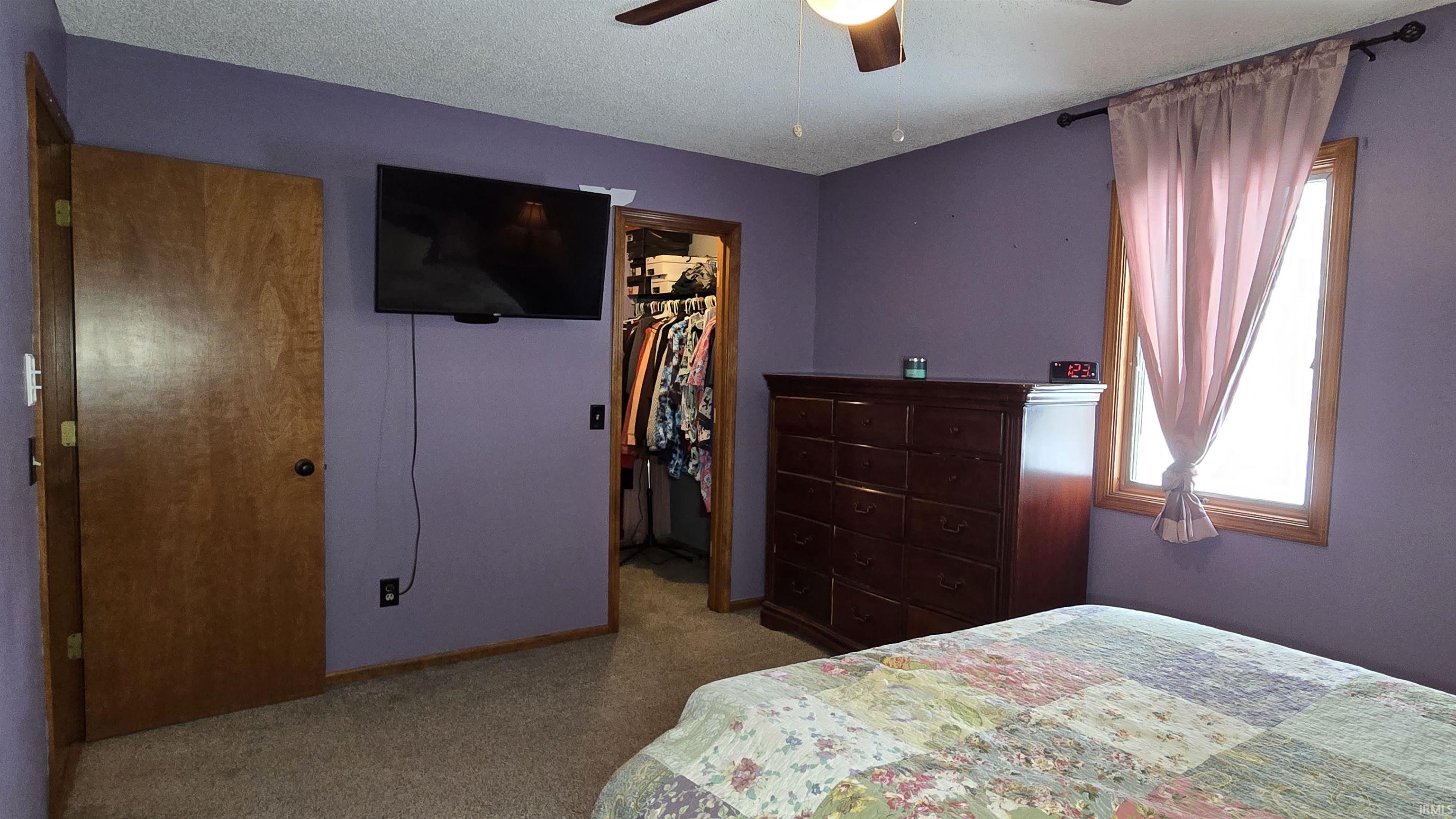 Bedroom featuring a spacious closet, carpet floors, a ceiling fan, and a textured ceiling
