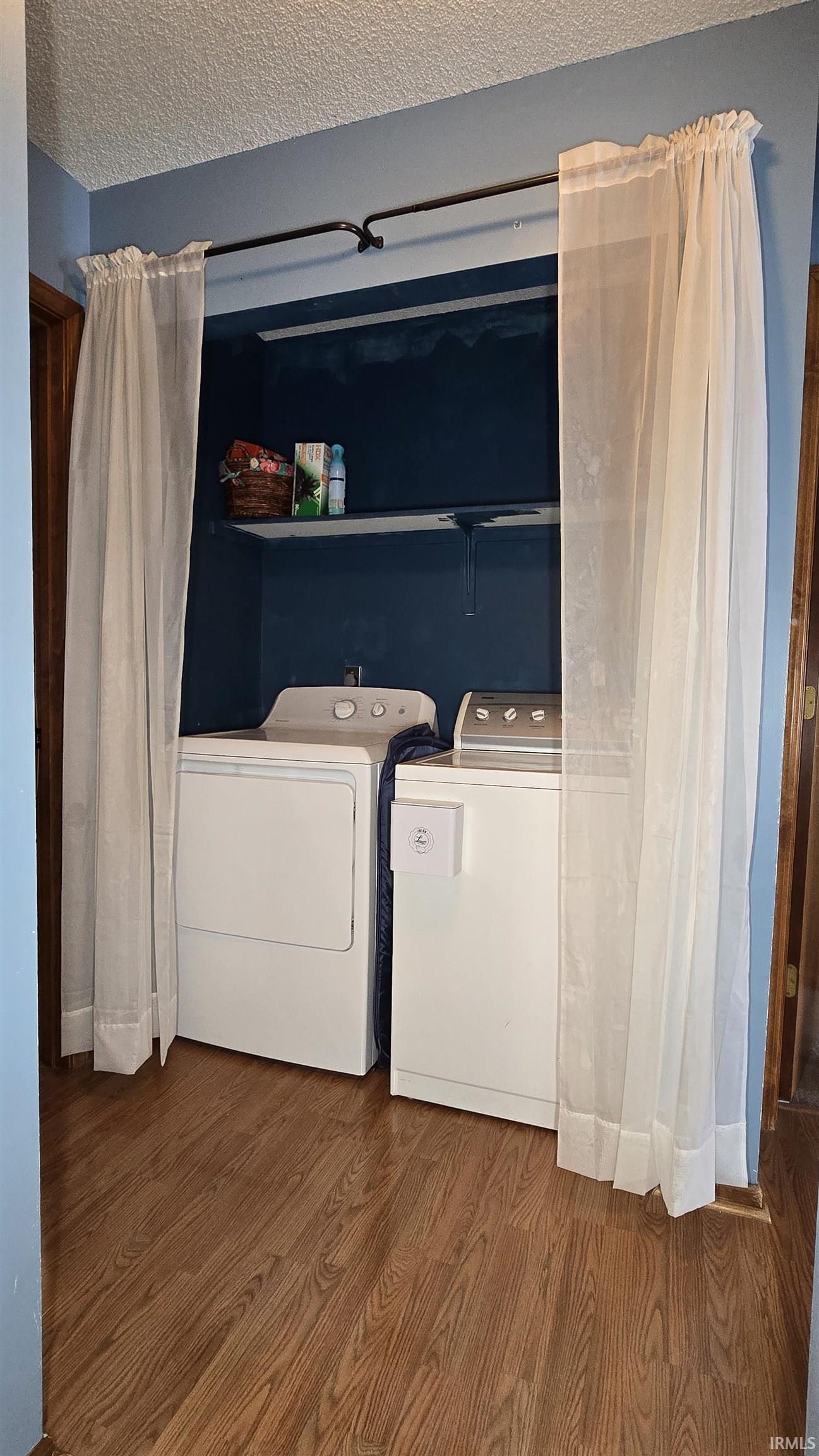 Laundry area with wood finished floors, washer and dryer, and a textured ceiling
