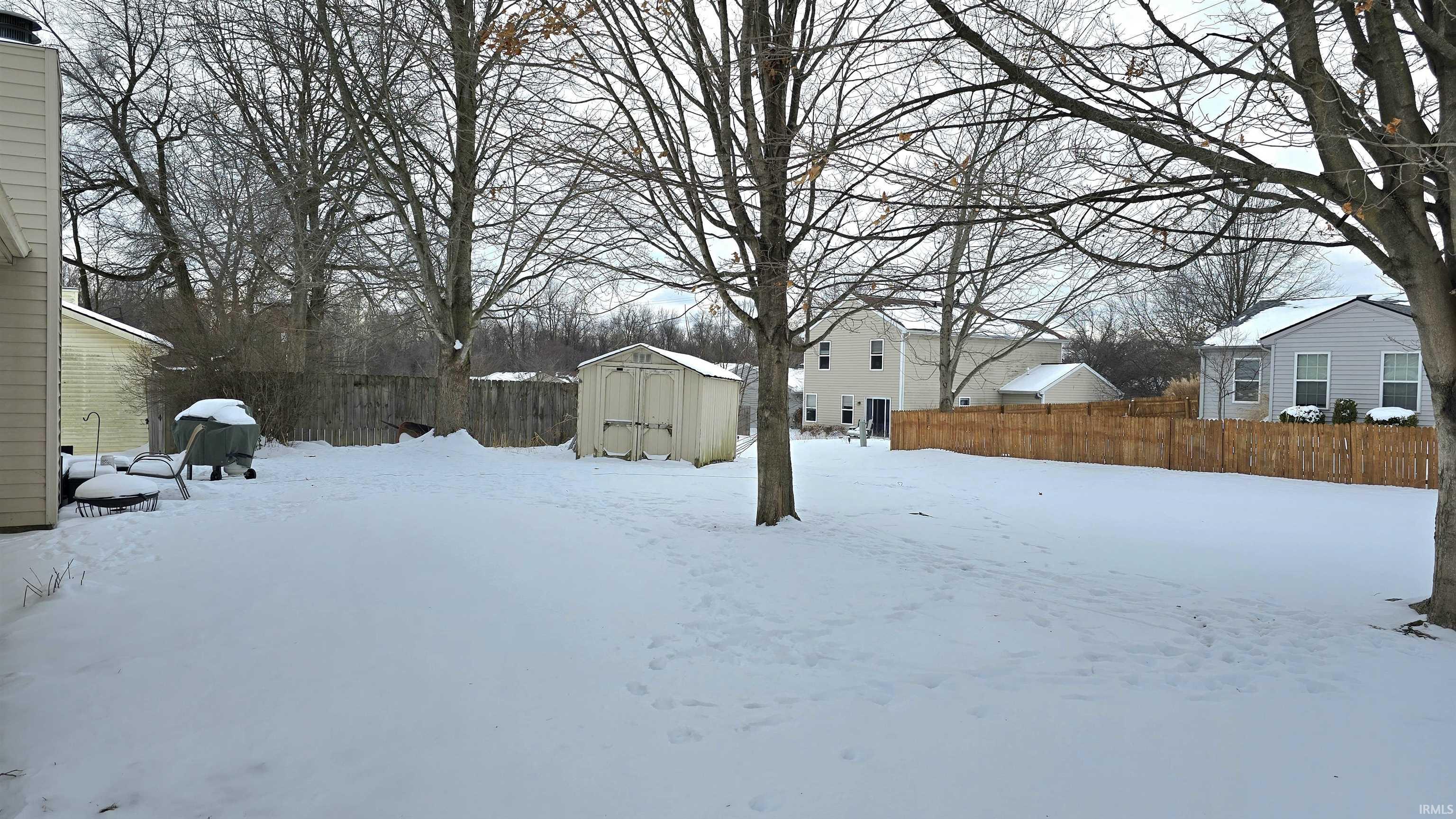 Yard layered in snow with a fenced backyard and a storage unit