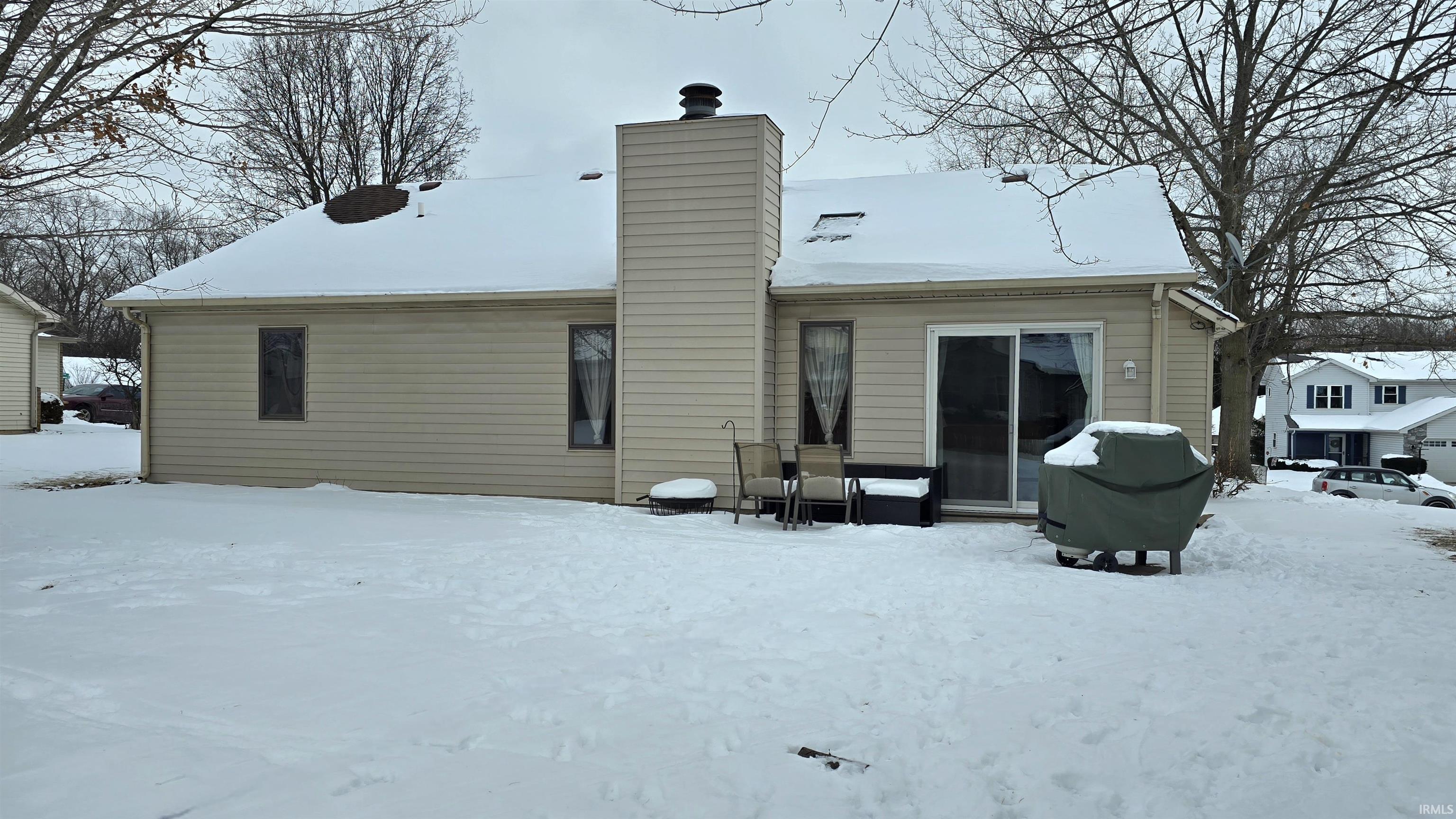 Snow covered back of property with a chimney and a patio area
