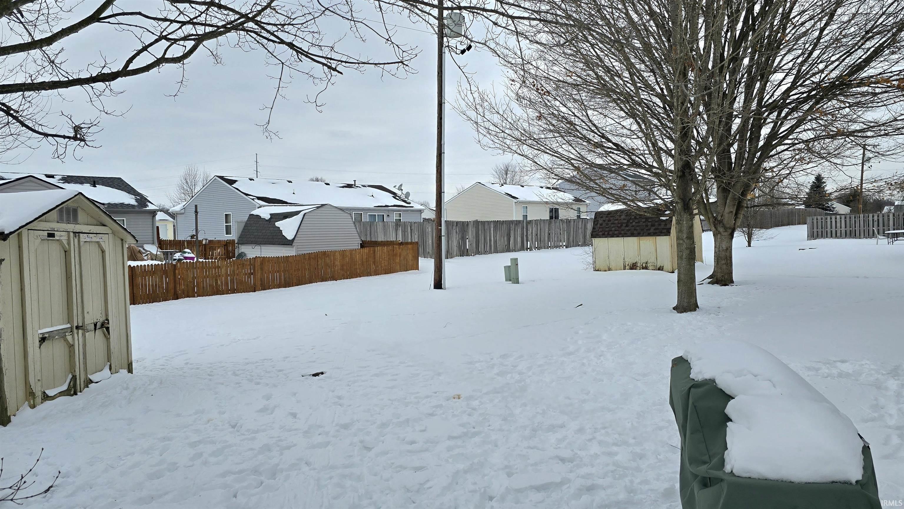 Snowy yard with a shed, a fenced backyard, and a residential view