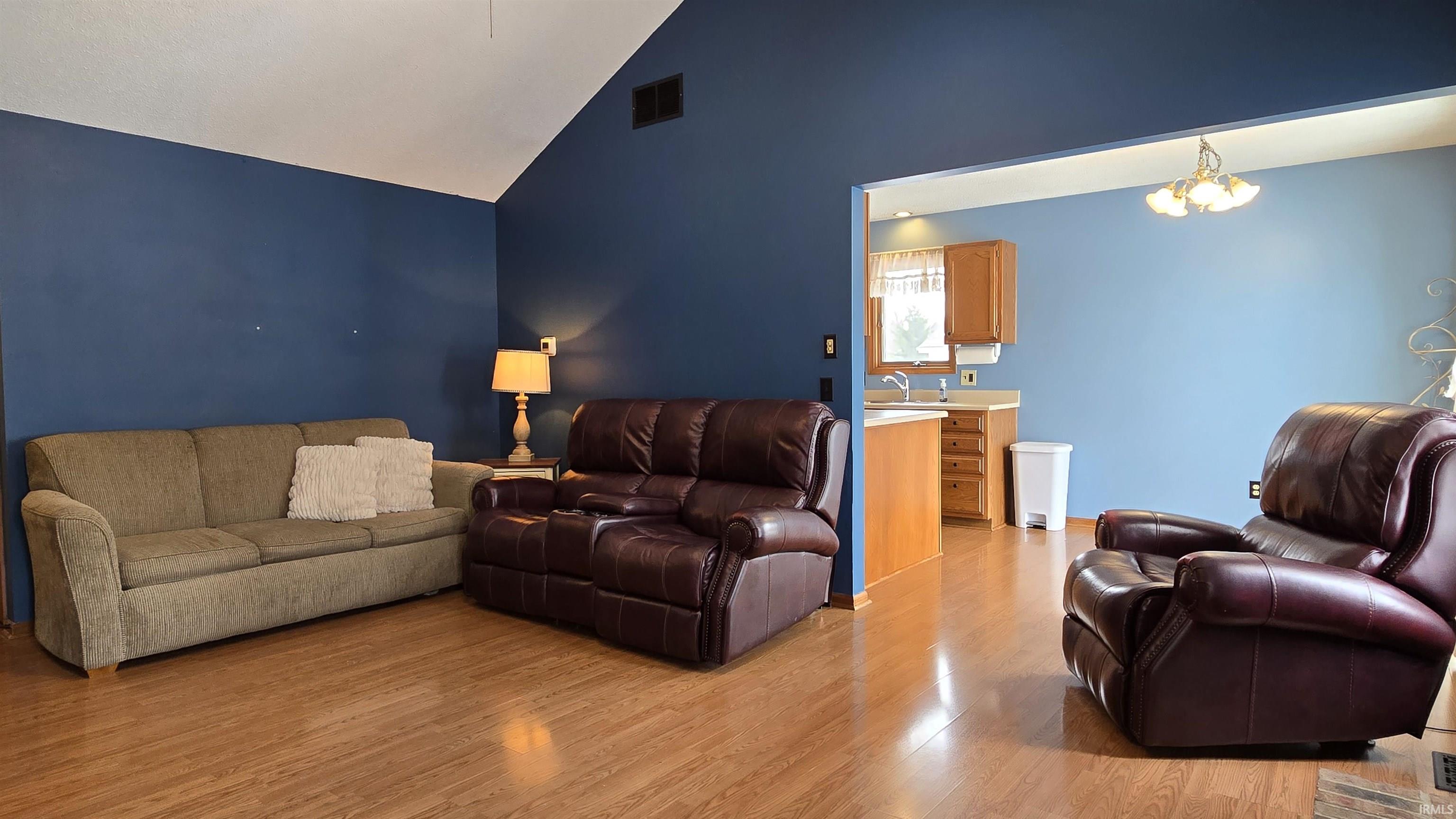 Living room featuring light wood-style floors, a chandelier, and high vaulted ceiling