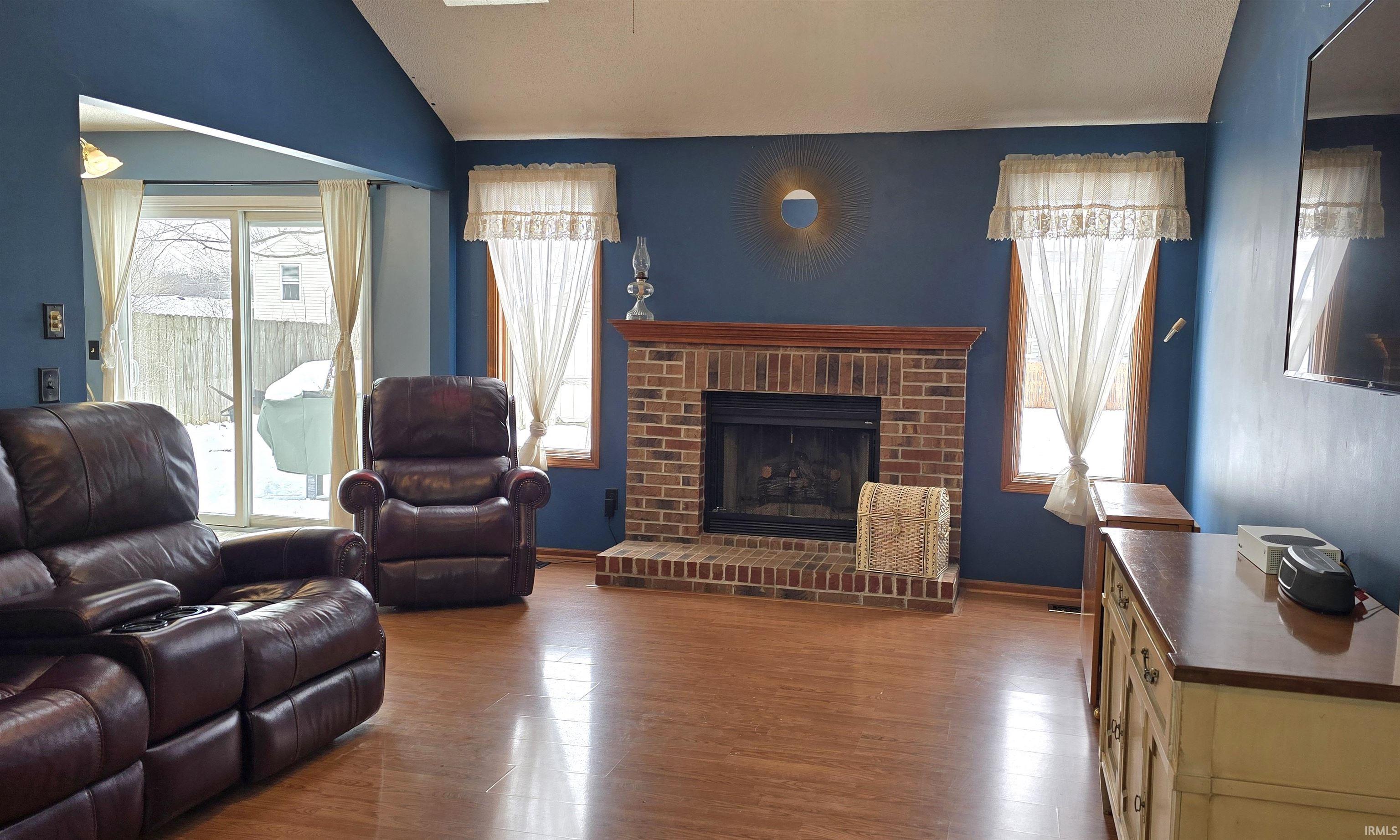 Living room with a brick fireplace, wood finished floors, and vaulted ceiling