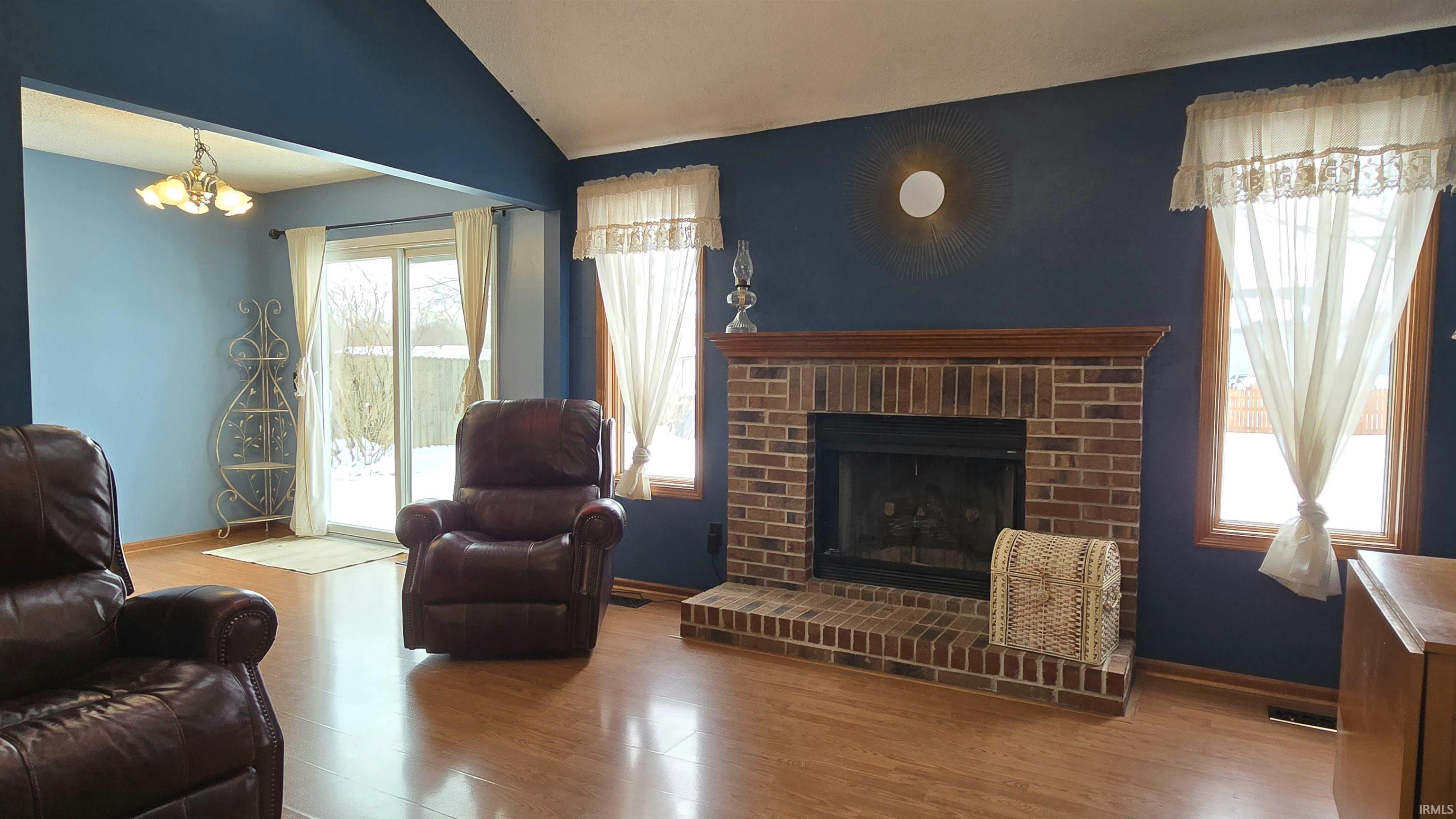 Living room featuring a fireplace, vaulted ceiling, wood finished floors, and a chandelier