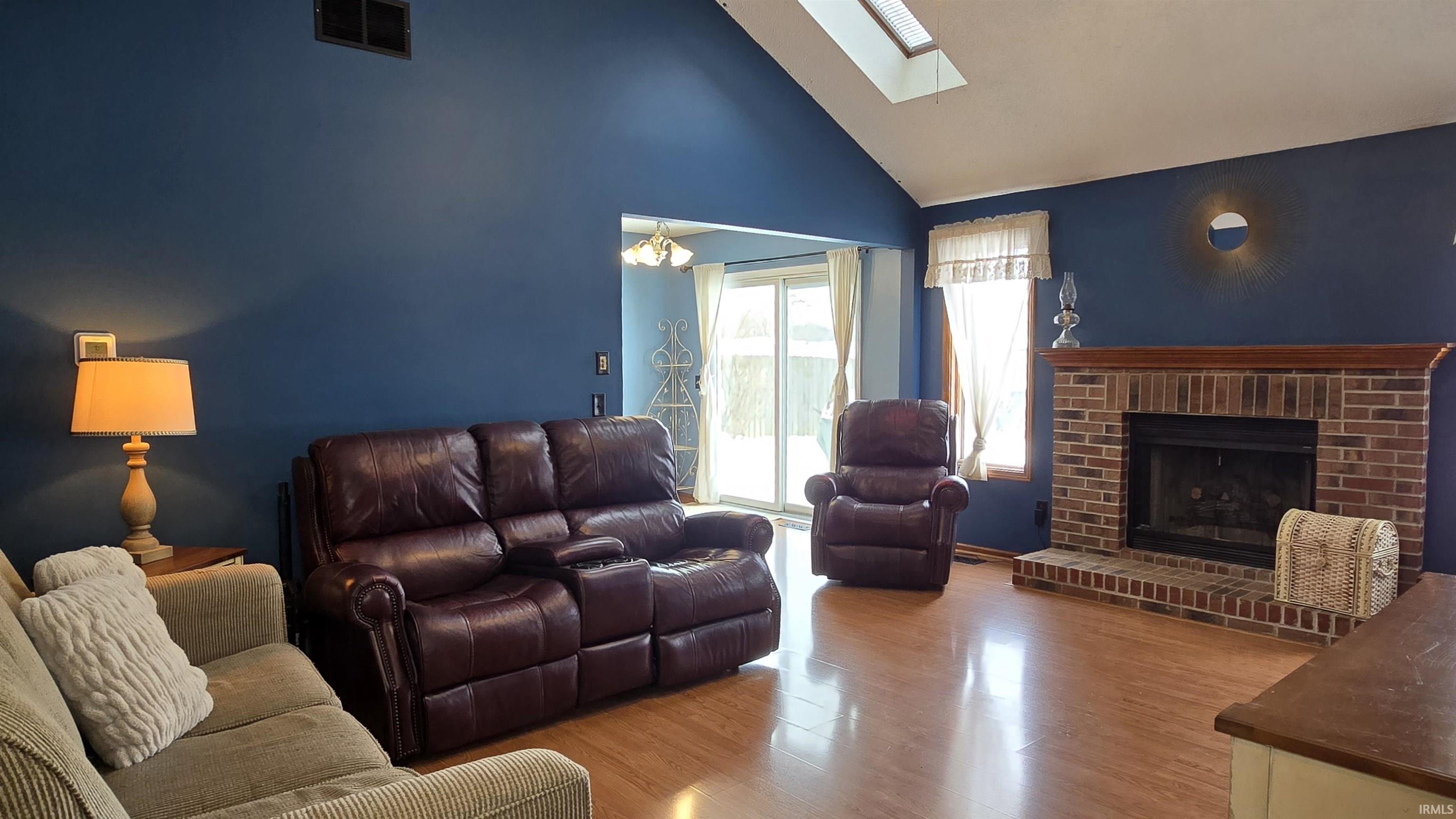 Living room featuring wood finished floors, a skylight, a fireplace, and high vaulted ceiling