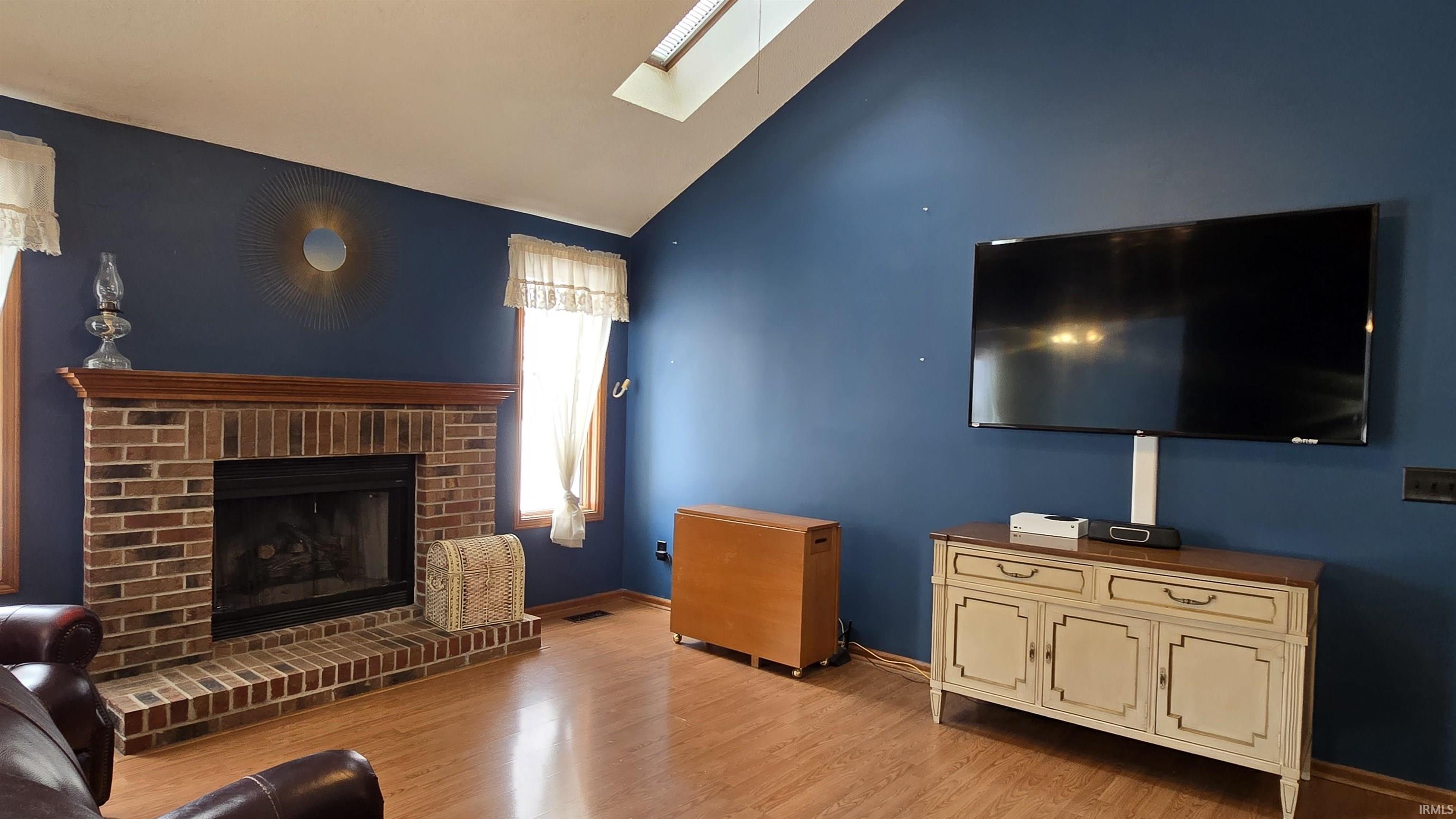 Living room with light wood finished floors, lofted ceiling, a skylight, and a fireplace