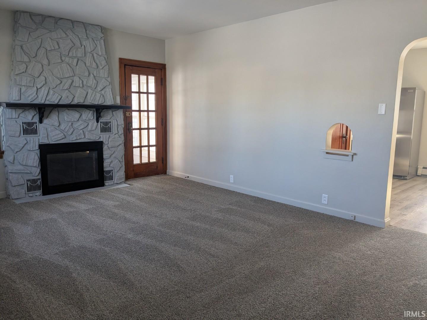Unfurnished living room featuring a fireplace, carpet flooring, and arched walkways
