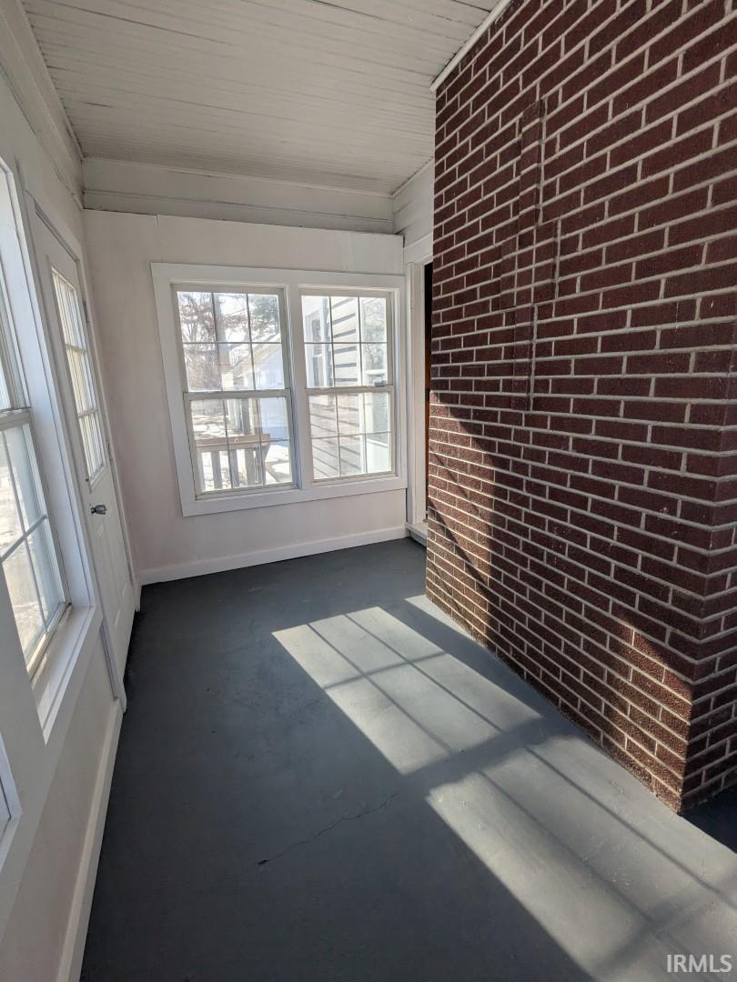 Unfurnished sunroom with brick wall and baseboards