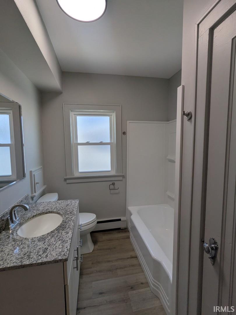 Full bath featuring vanity, light wood-style flooring, a baseboard heating unit, and bathing tub / shower combination