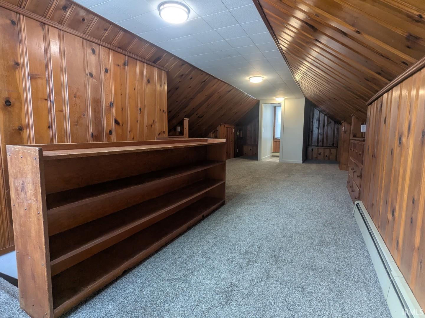 Additional living space featuring a baseboard radiator, light colored carpet, wooden walls, and lofted ceiling