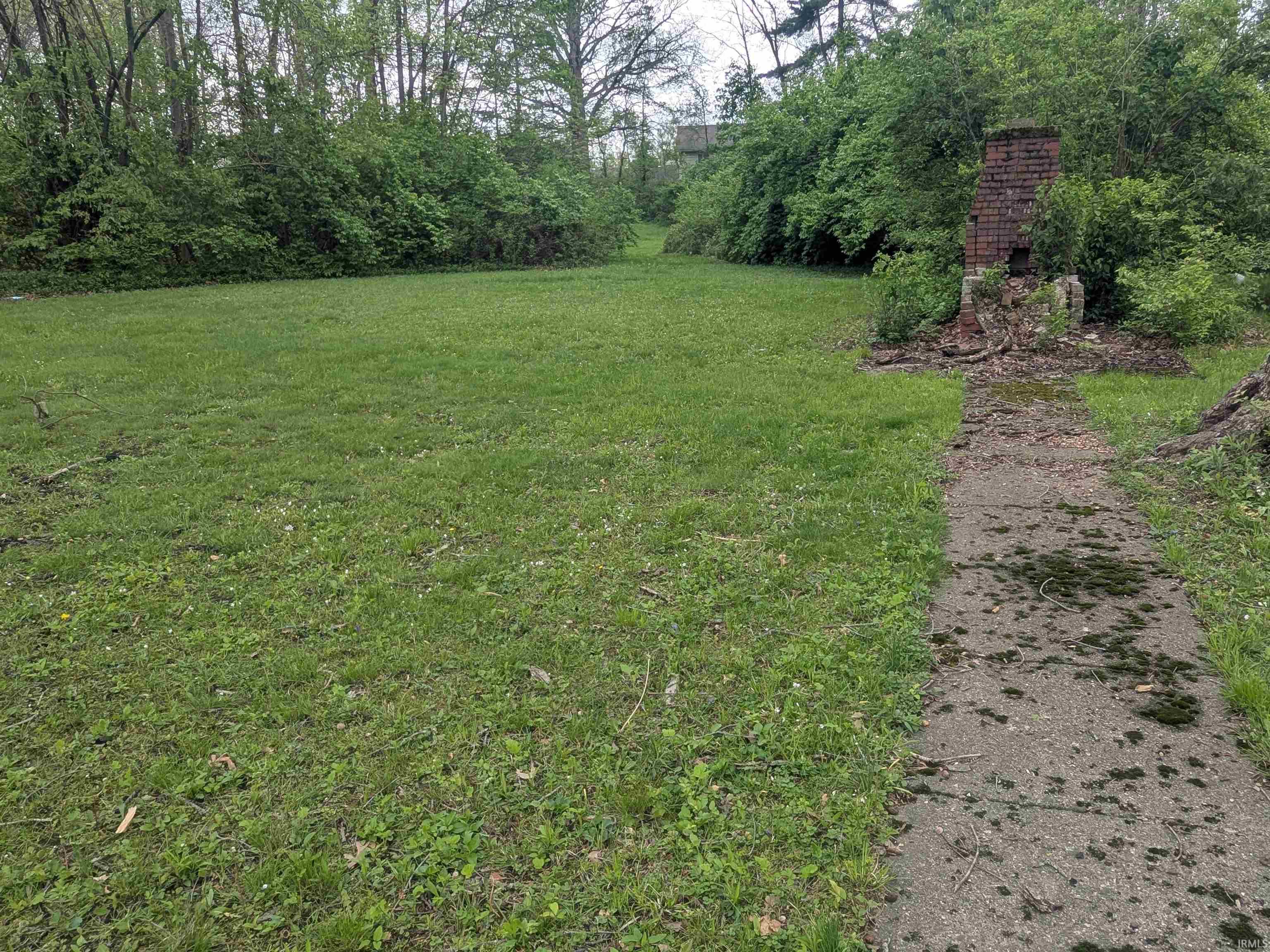 Expansive green space featuring a concrete pathway, mature perimeter trees, and established shrubbery