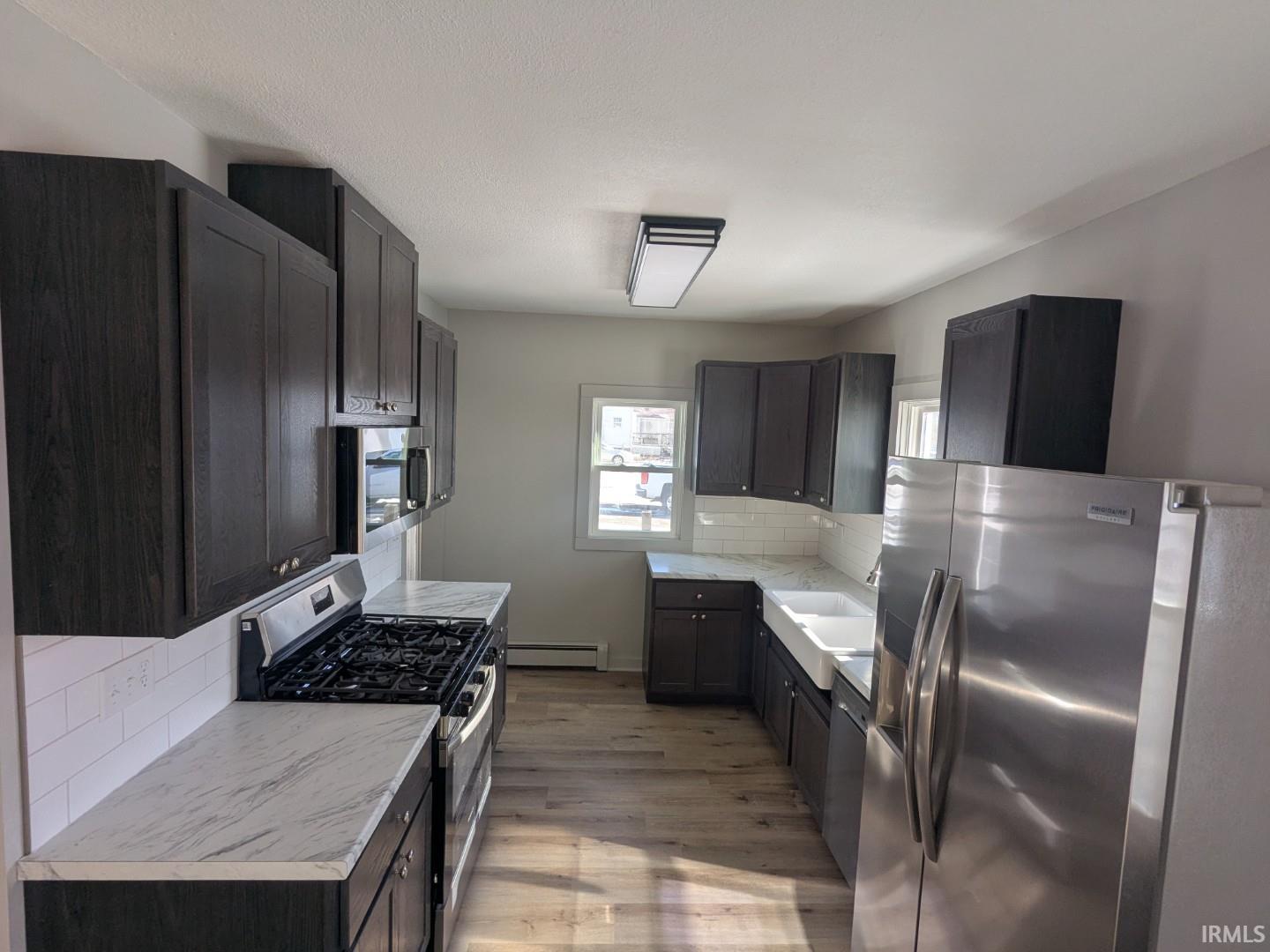 Kitchen with stainless steel appliances, decorative backsplash, light wood-style floors, a baseboard heating unit, and dark brown cabinetry