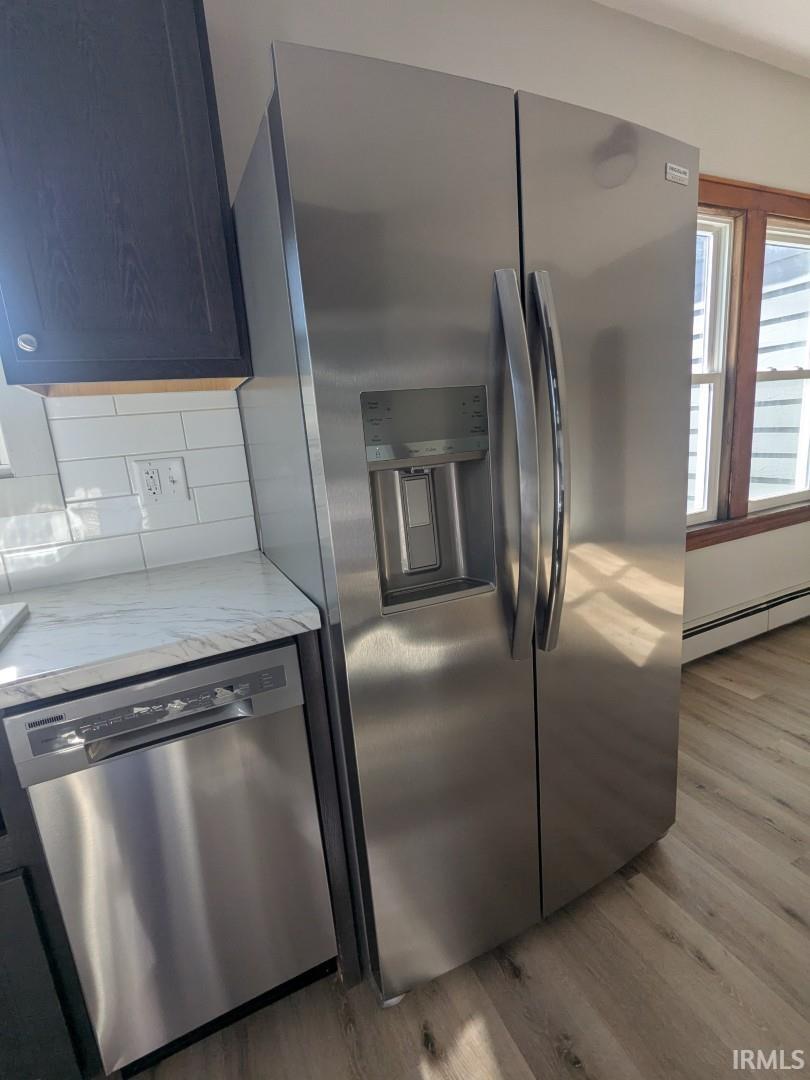 Kitchen featuring stainless steel appliances, light wood-type flooring, a baseboard heating unit, decorative backsplash, and light stone counters