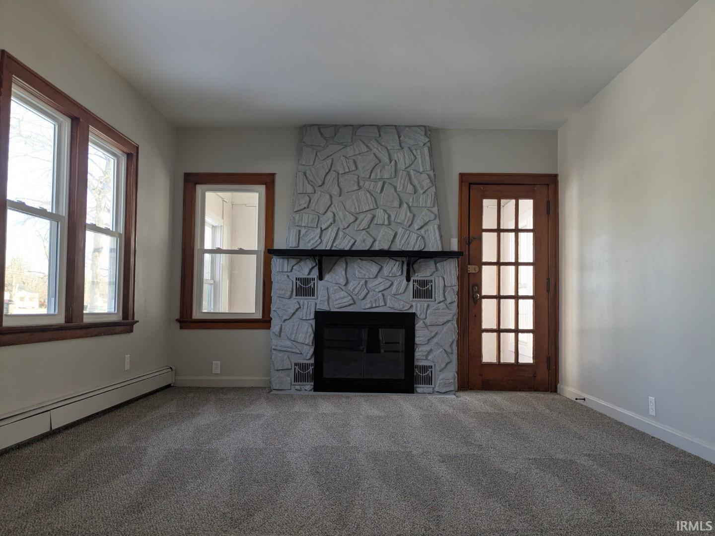 Unfurnished living room featuring a stone fireplace and carpet floors