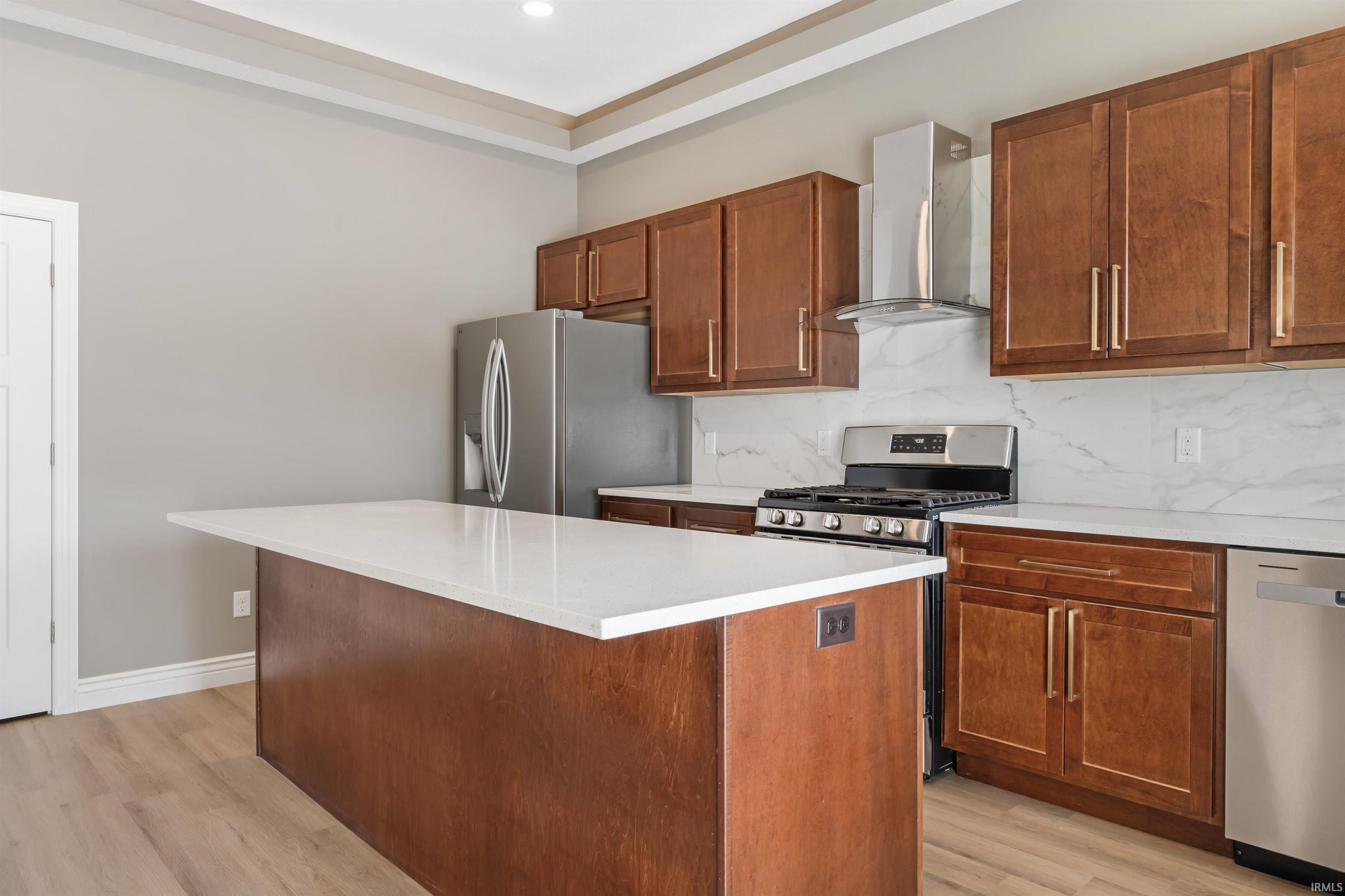 Kitchen with backsplash, extractor fan, appliances with stainless steel finishes, a center island, and light wood-type flooring