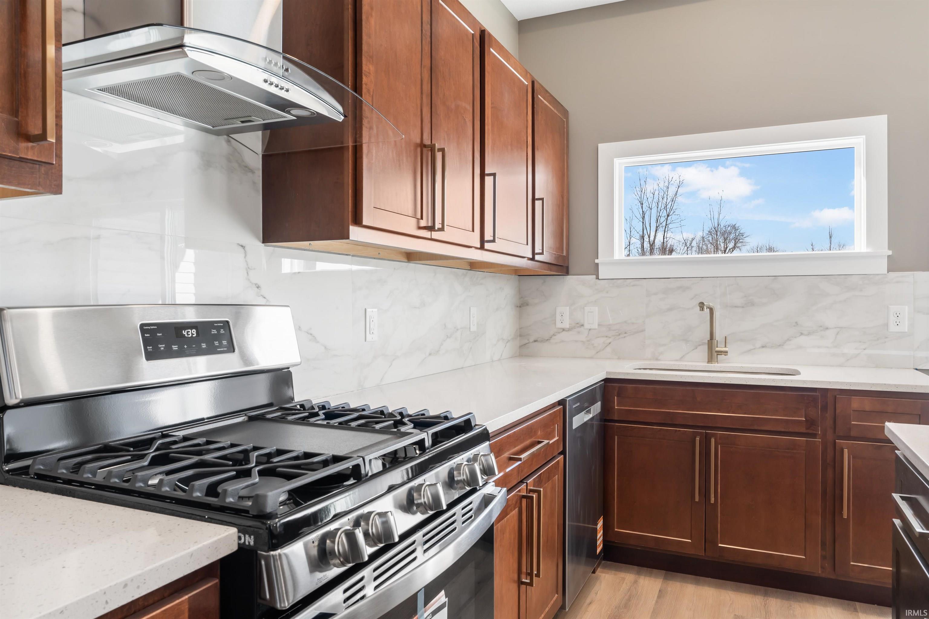 Kitchen featuring appliances with stainless steel finishes, extractor fan, decorative backsplash, light stone counters, and light wood-style floors