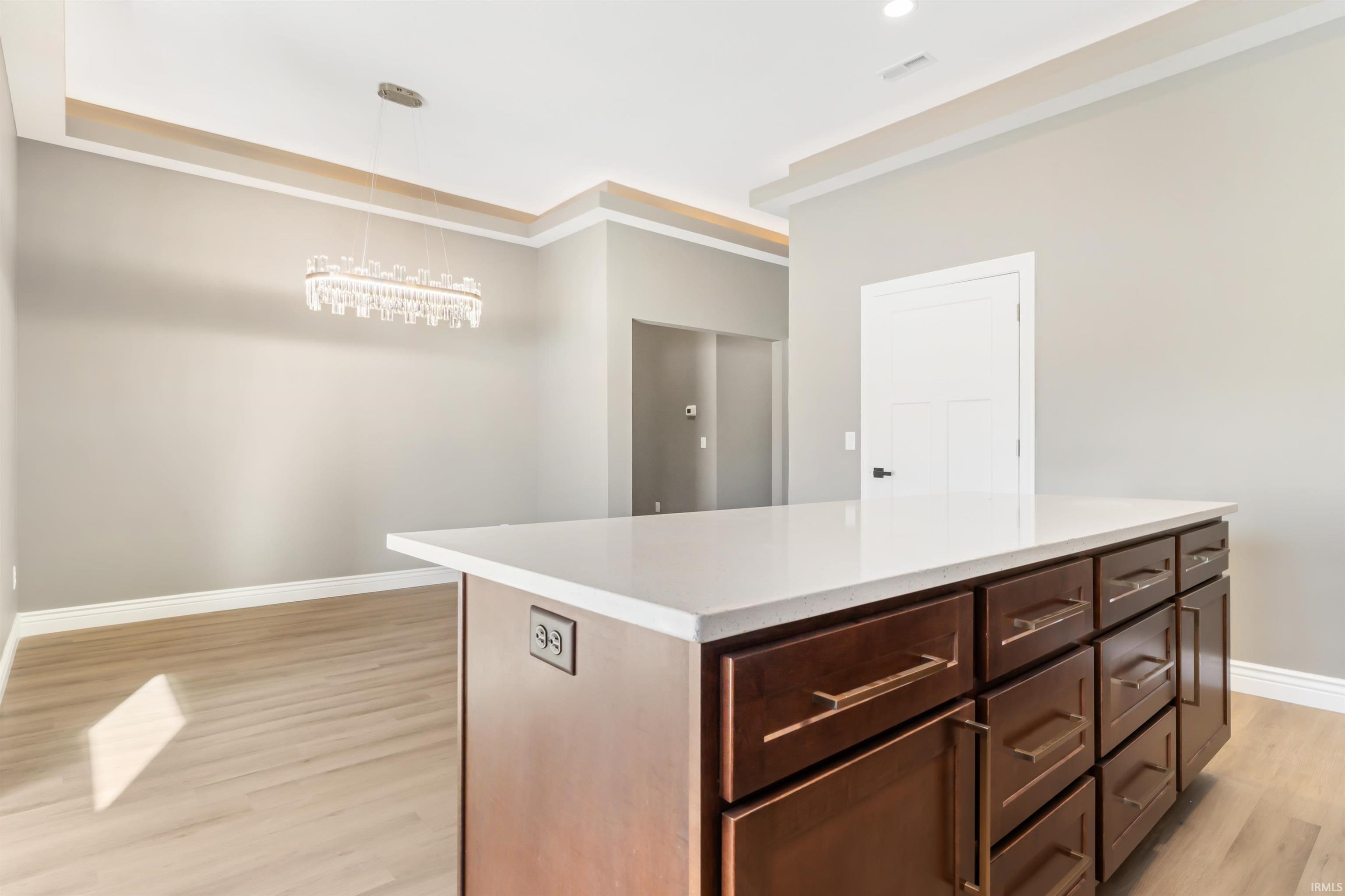 Kitchen featuring a center island, decorative light fixtures, light wood-style flooring, dark brown cabinets, and light stone countertops