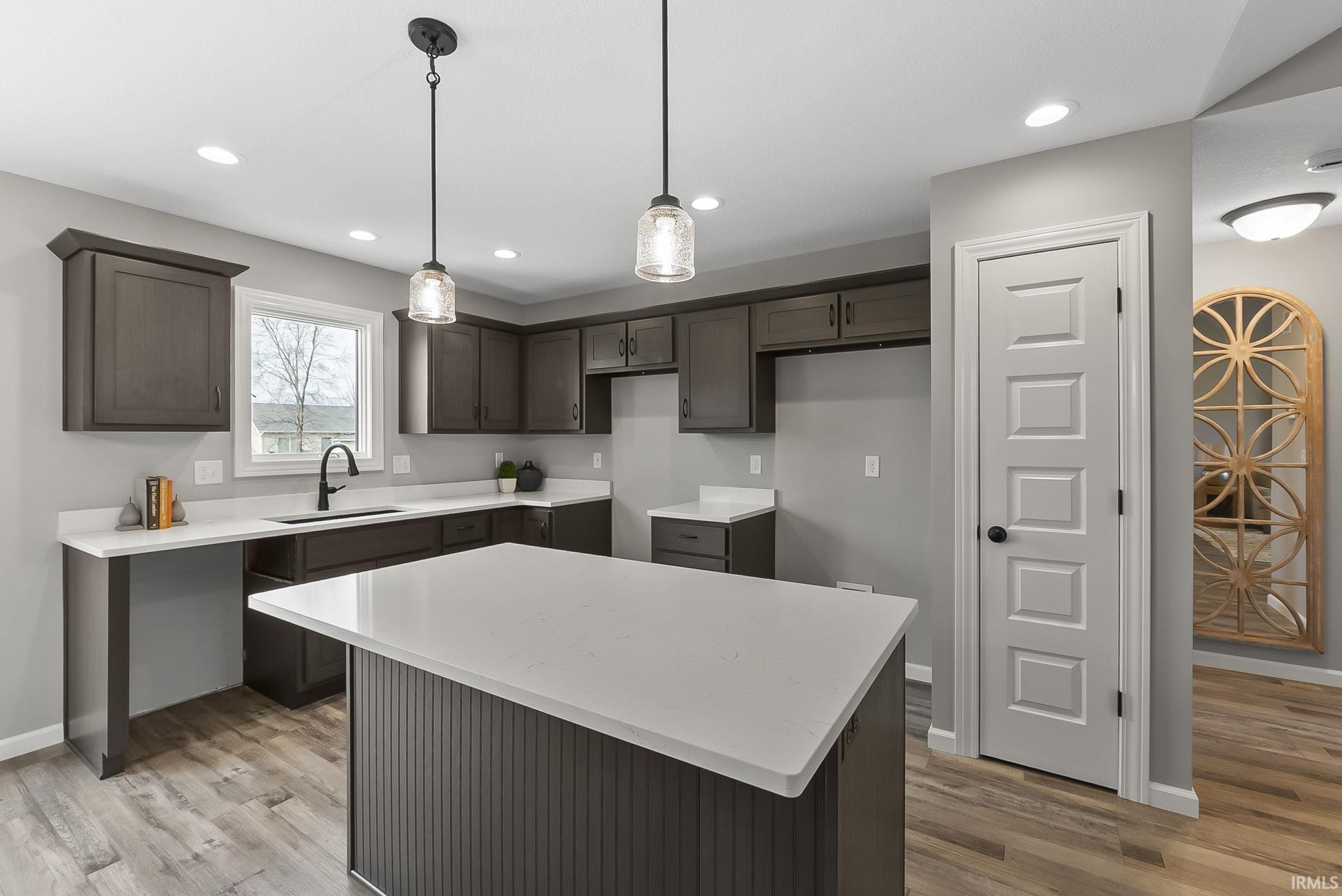 Kitchen featuring dark wood finish cabinets, light wood finished floors, decorative light fixtures, a kitchen island, and light stone countertops