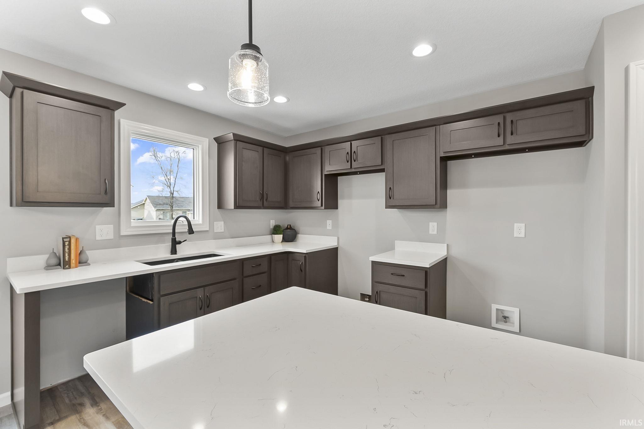 Kitchen featuring dark wood finish cabinetry, wood finished floors, light stone countertops, and pendant lighting
