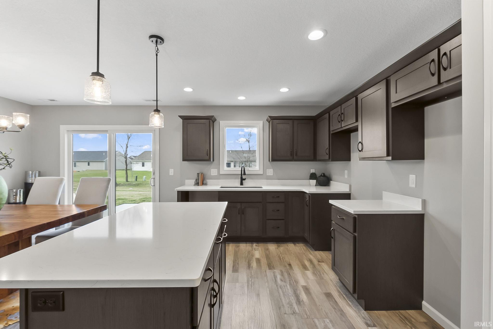 Kitchen with dark wood finish cabinets, light wood-style flooring, decorative light fixtures, a kitchen island, and light stone counters