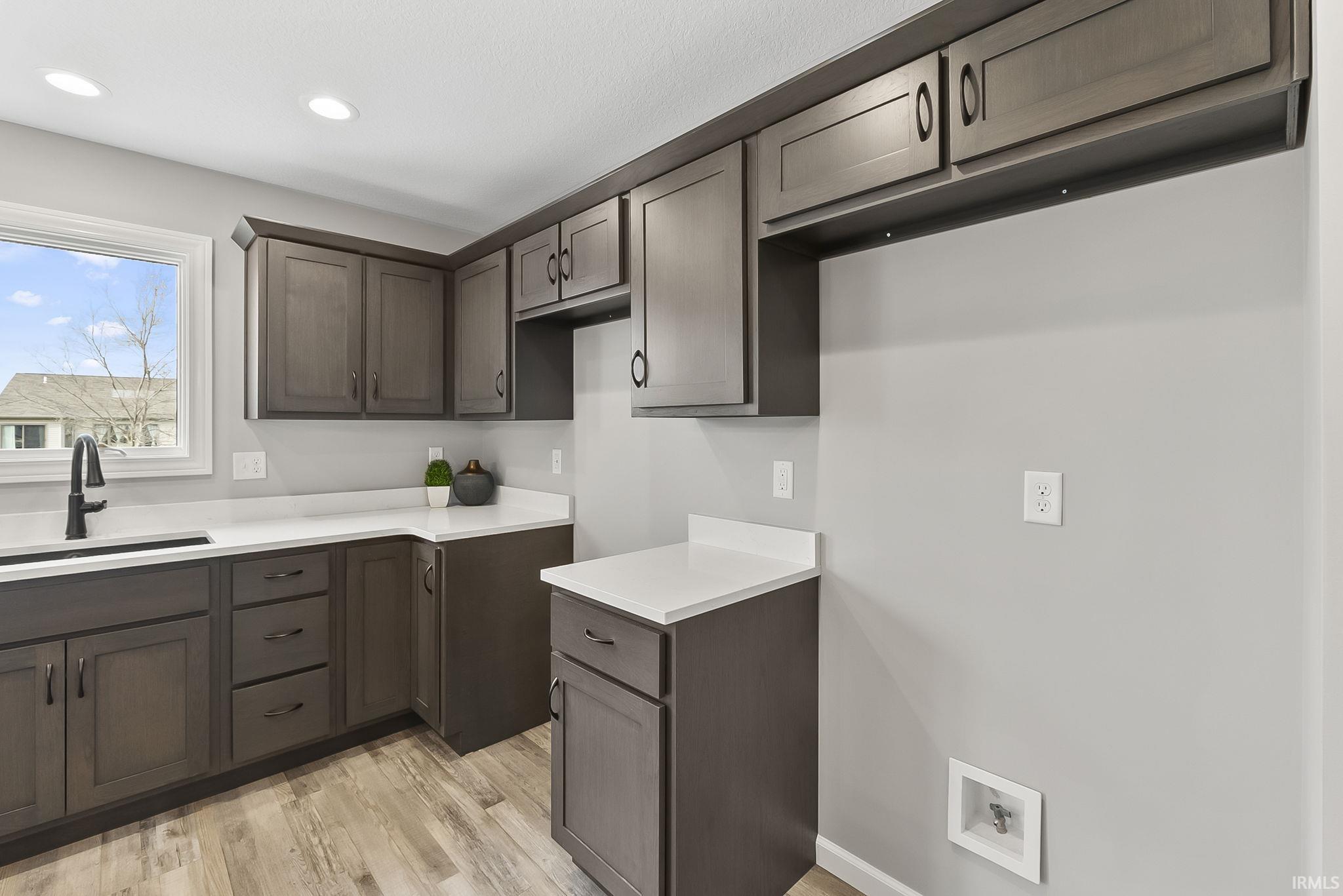 Kitchen featuring light countertops, light wood-type flooring, dark wood finish cabinetry, and recessed lighting