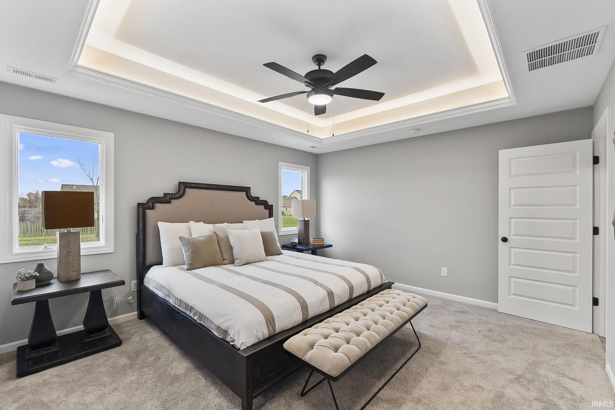 Carpeted bedroom featuring ceiling fan and a raised ceiling