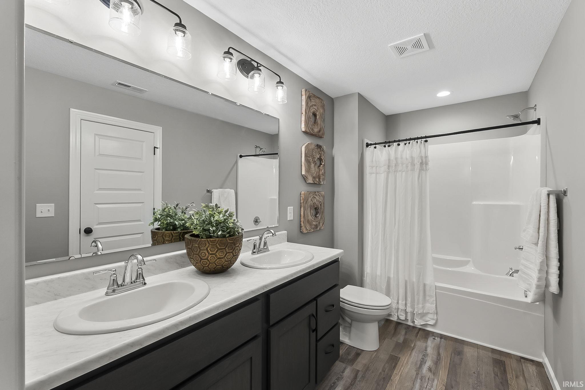 Bathroom with double vanity, dark wood finished floors, shower / bath combo, and a textured ceiling