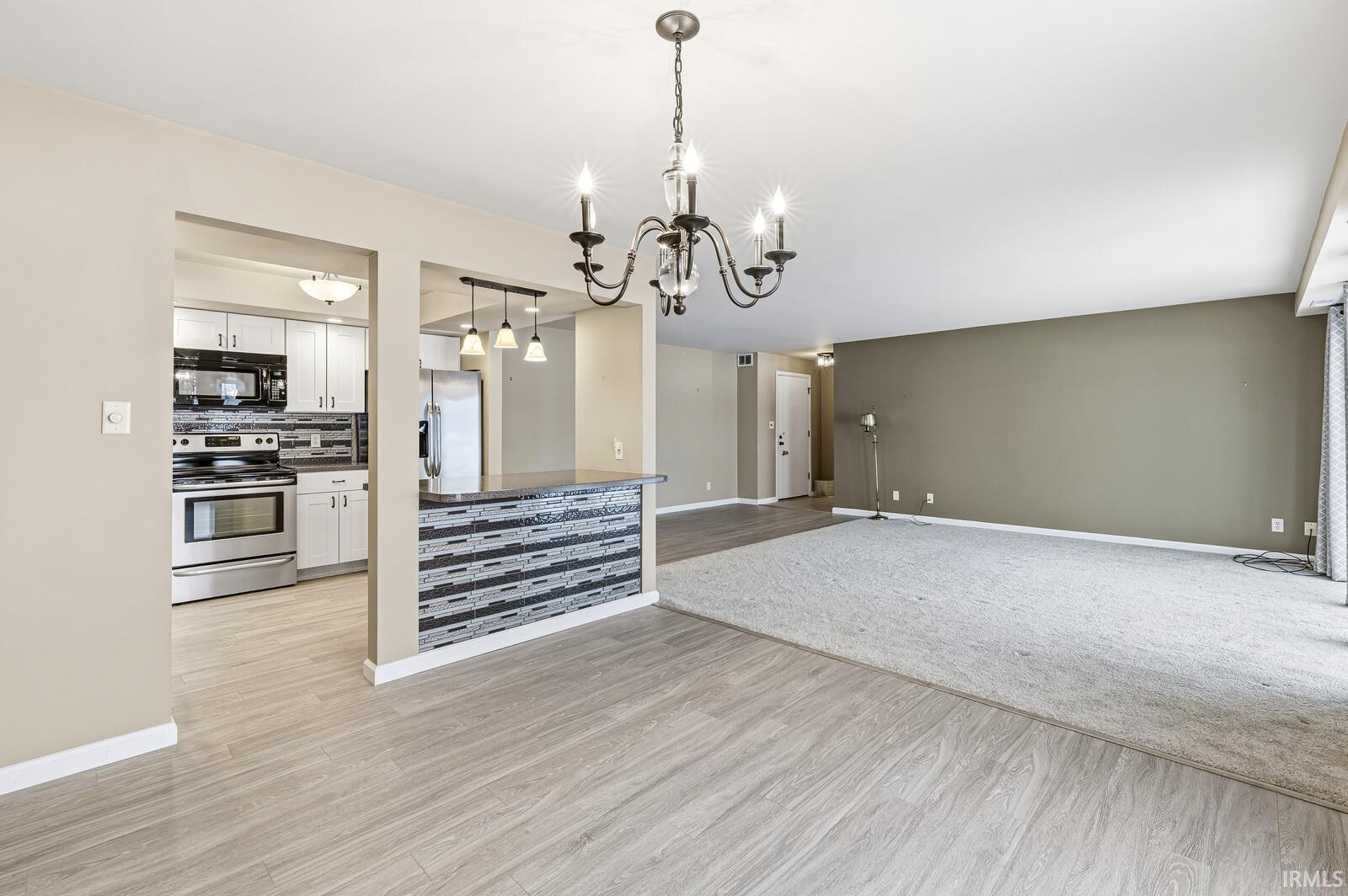 Kitchen featuring stainless steel appliances, open floor plan, white cabinets, tasteful backsplash, and suspended lighting