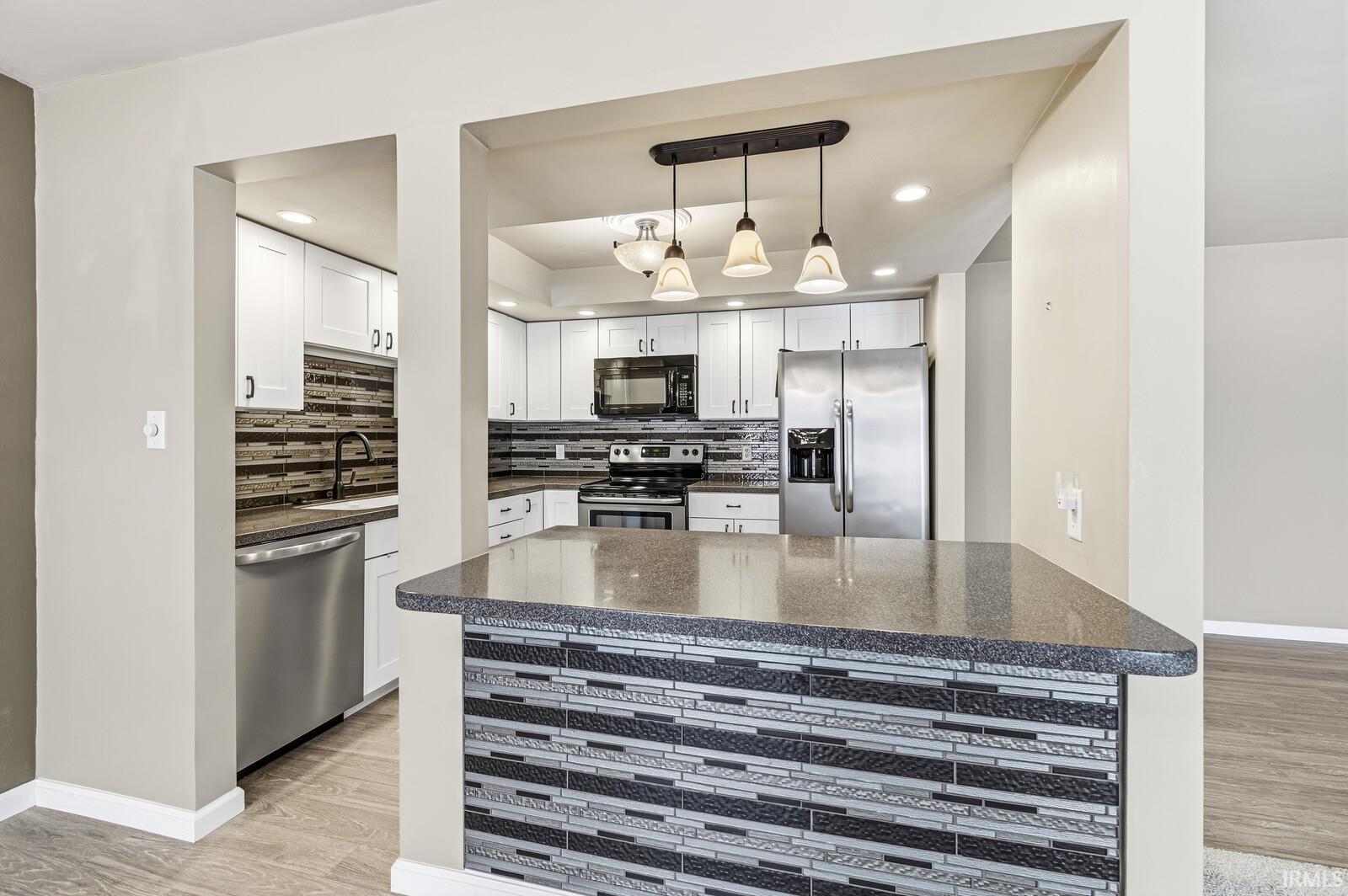 Kitchen with stainless steel appliances, tasteful backsplash, dark stone countertops, pendant lighting, and white cabinetry