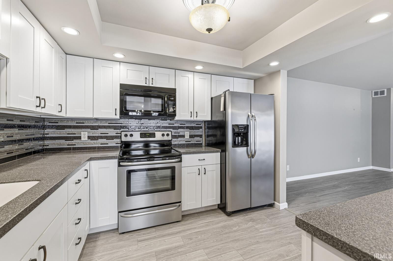 Kitchen with recessed lighting, stainless steel appliances, white cabinetry, light wood-style floors, and backsplash