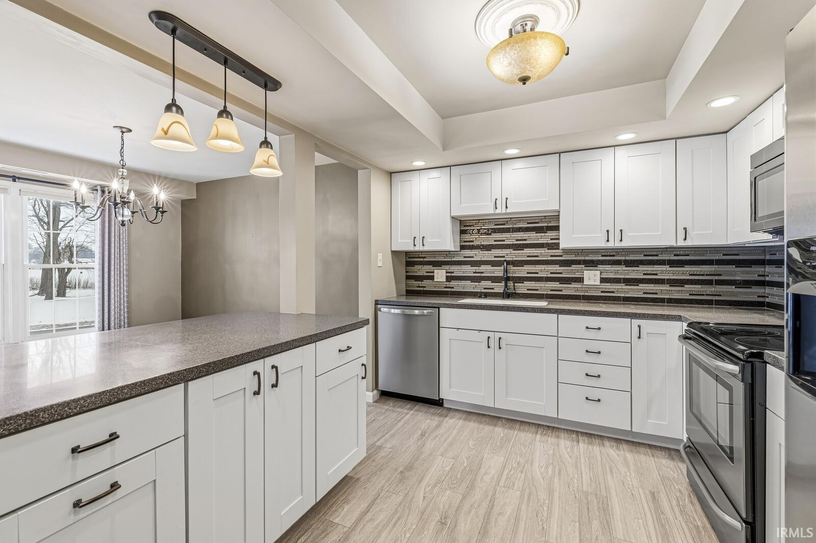 Kitchen with stainless steel appliances, white cabinetry, light wood-style flooring, dark stone countertops, and a raised ceiling