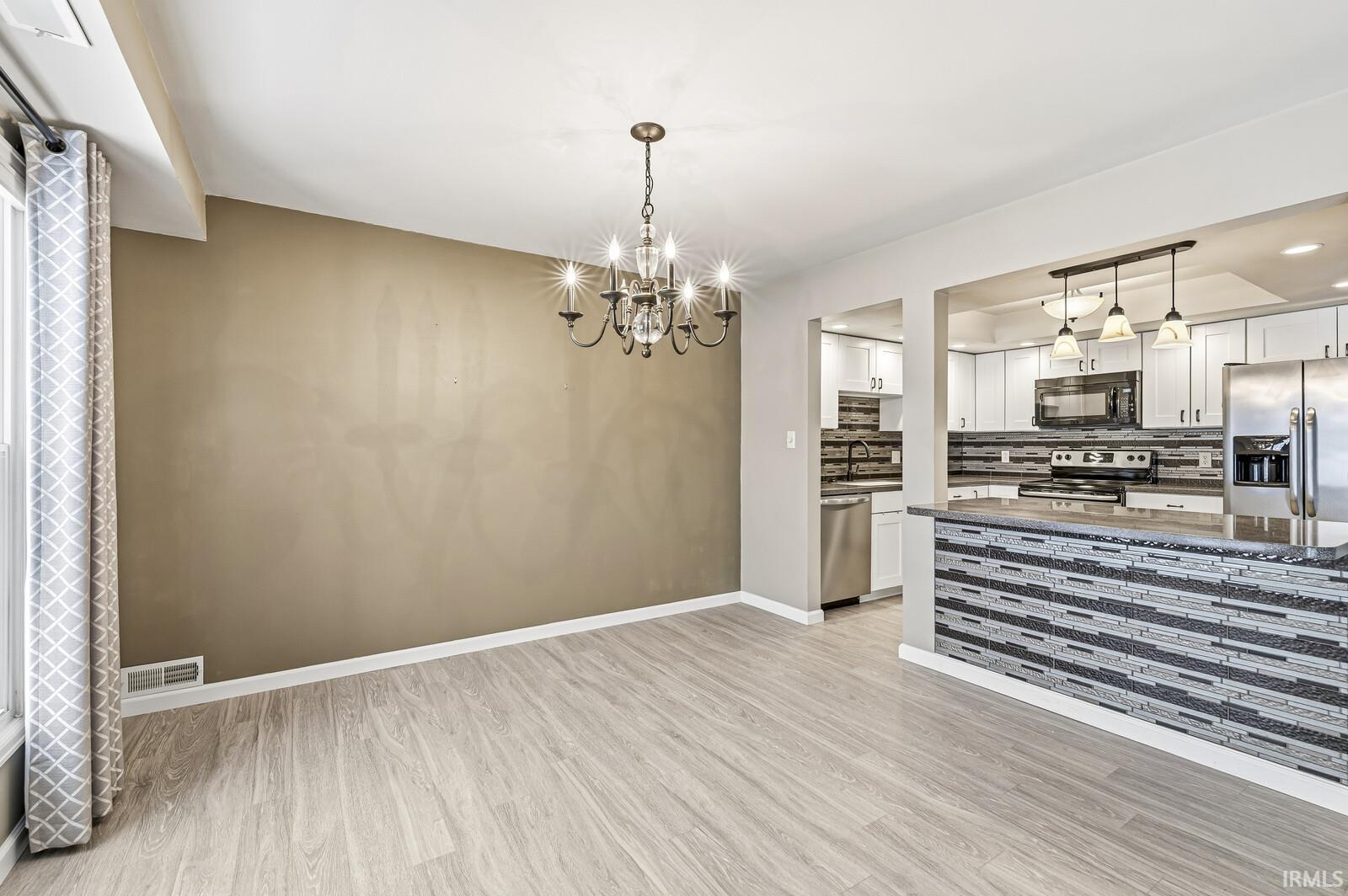 Kitchen featuring white cabinets, stainless steel appliances, dark stone counters, light wood-style floors, and backsplash