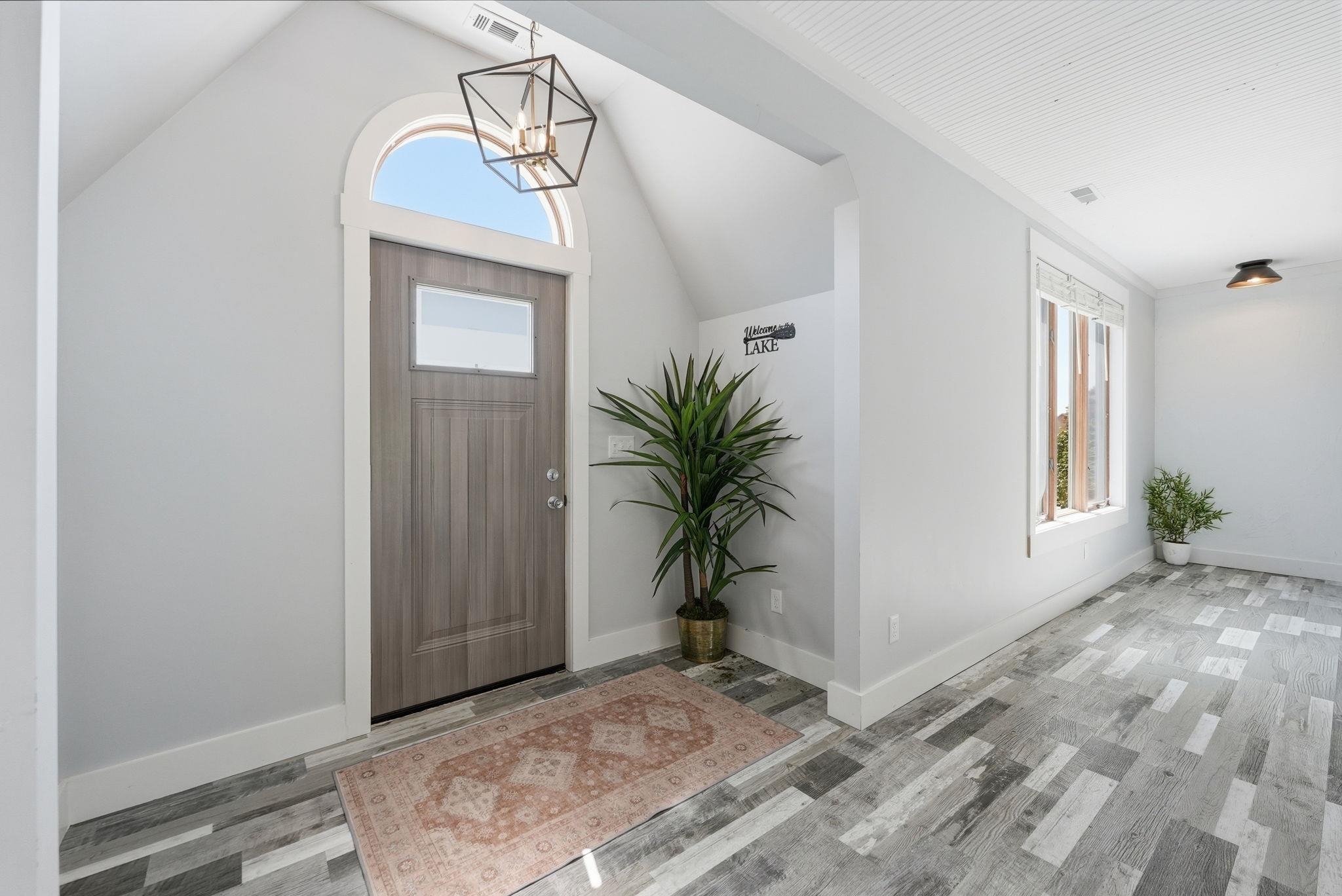 Entryway featuring a wood-finish door with an arched transom window, a geometric pendant light fixture, wood-finish flooring, and a window with blinds