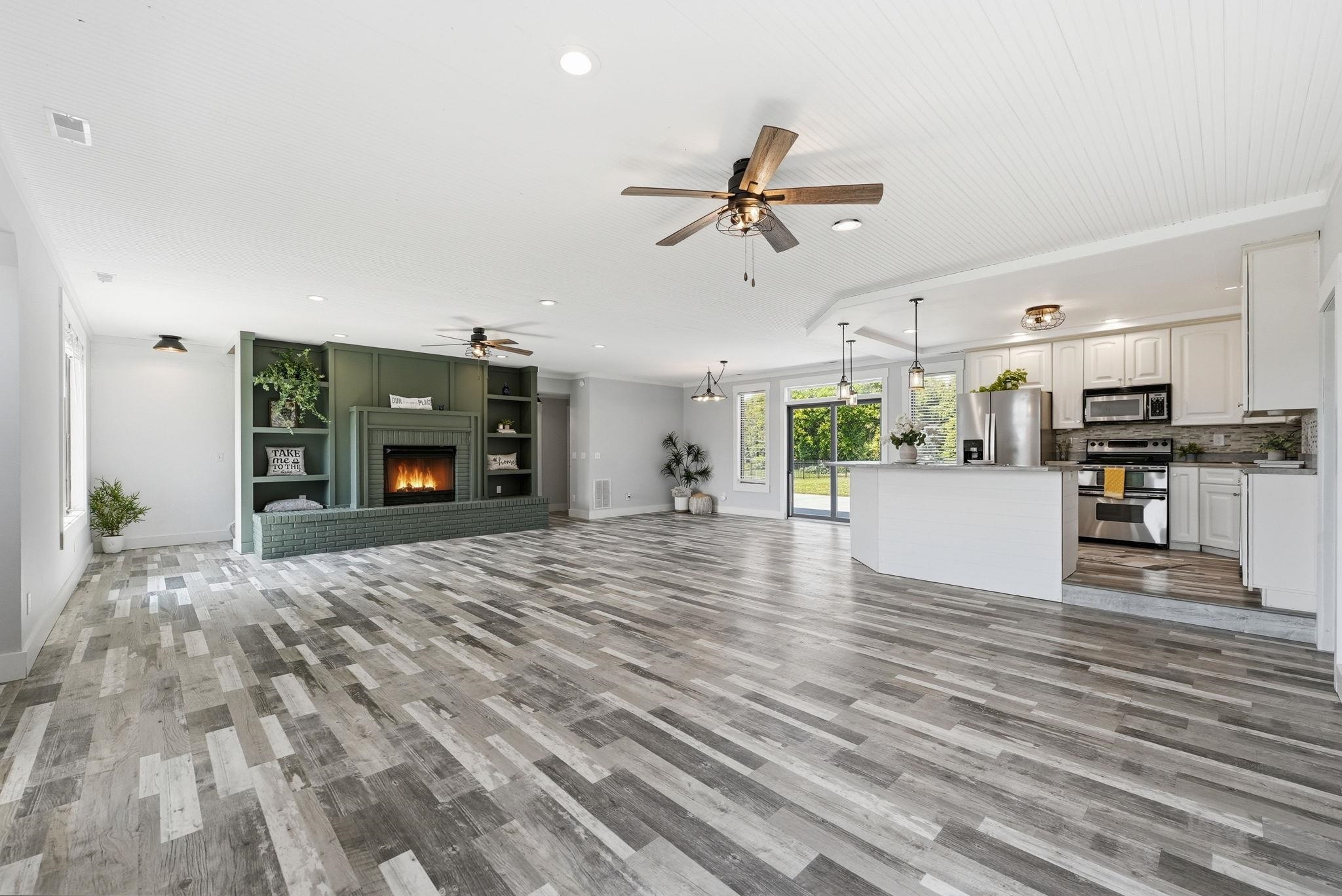 Spacious open-concept interior featuring wood-finish flooring, a built-in fireplace with shelving, a kitchen island, stainless steel appliances, and a beadboard ceiling