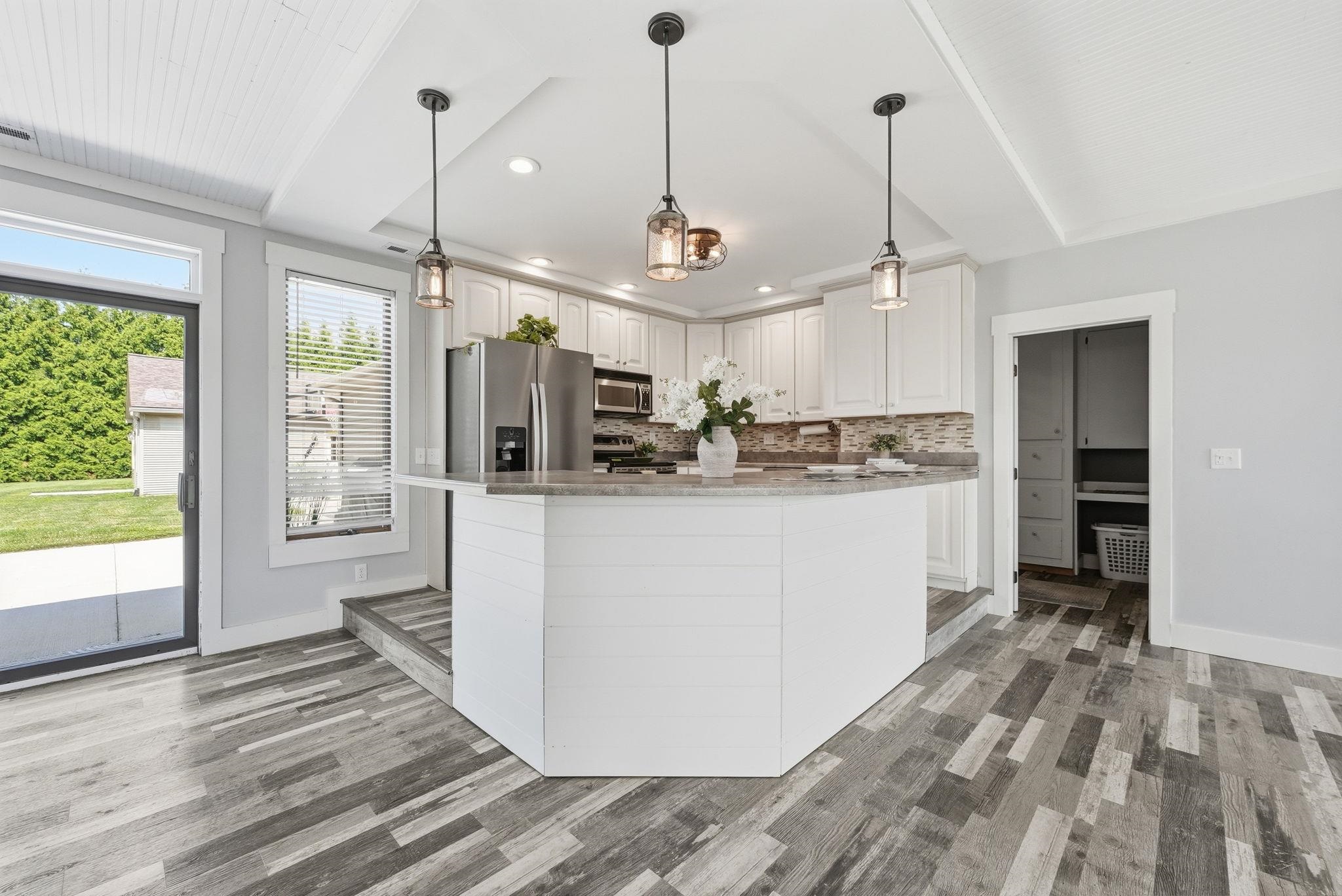 Kitchen featuring a multi-level island with seating, white shaker cabinetry, stainless steel appliances, and a tiled backsplash