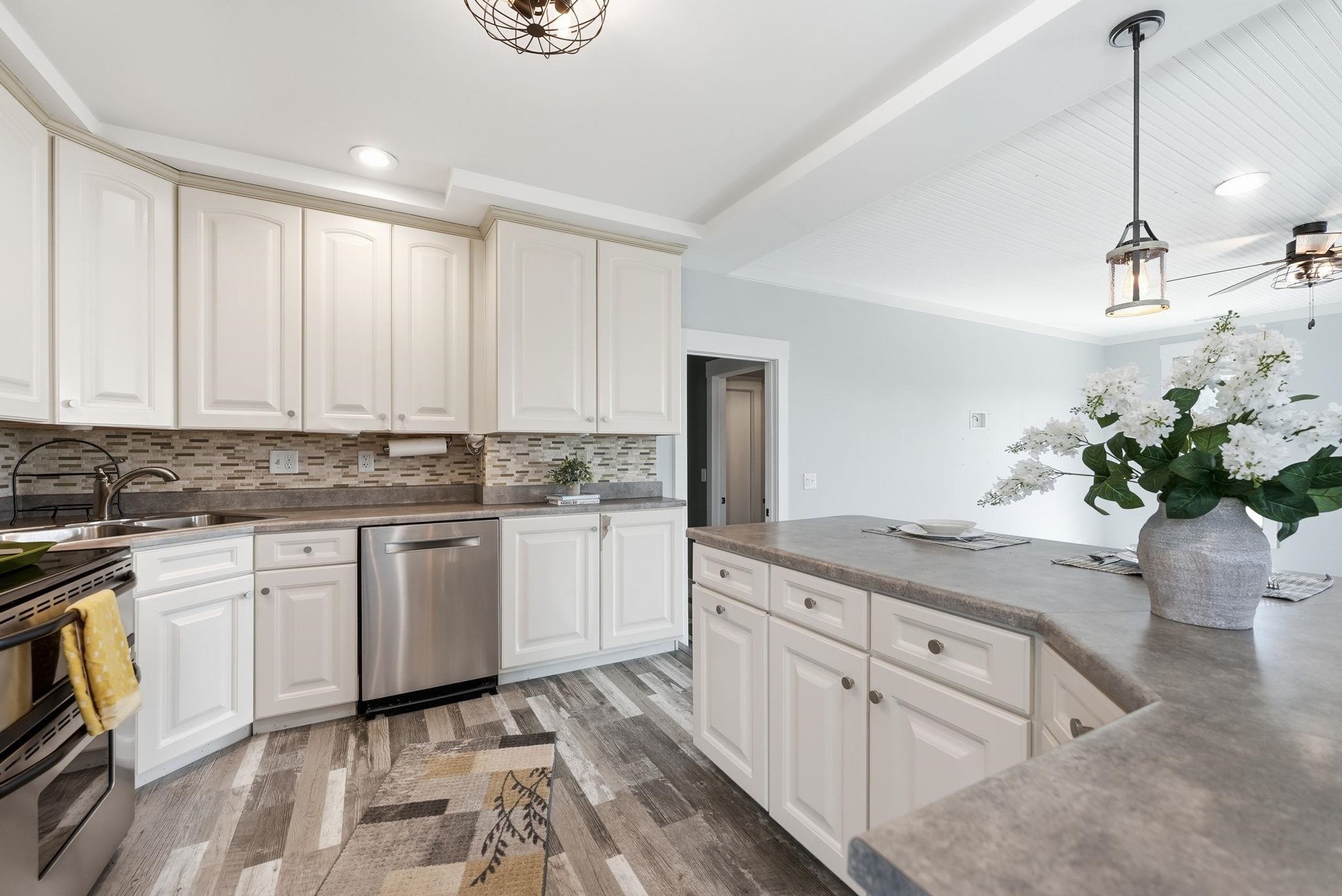 Open-concept kitchen featuring white shaker-style cabinetry, stainless steel appliances, and a tile backsplash