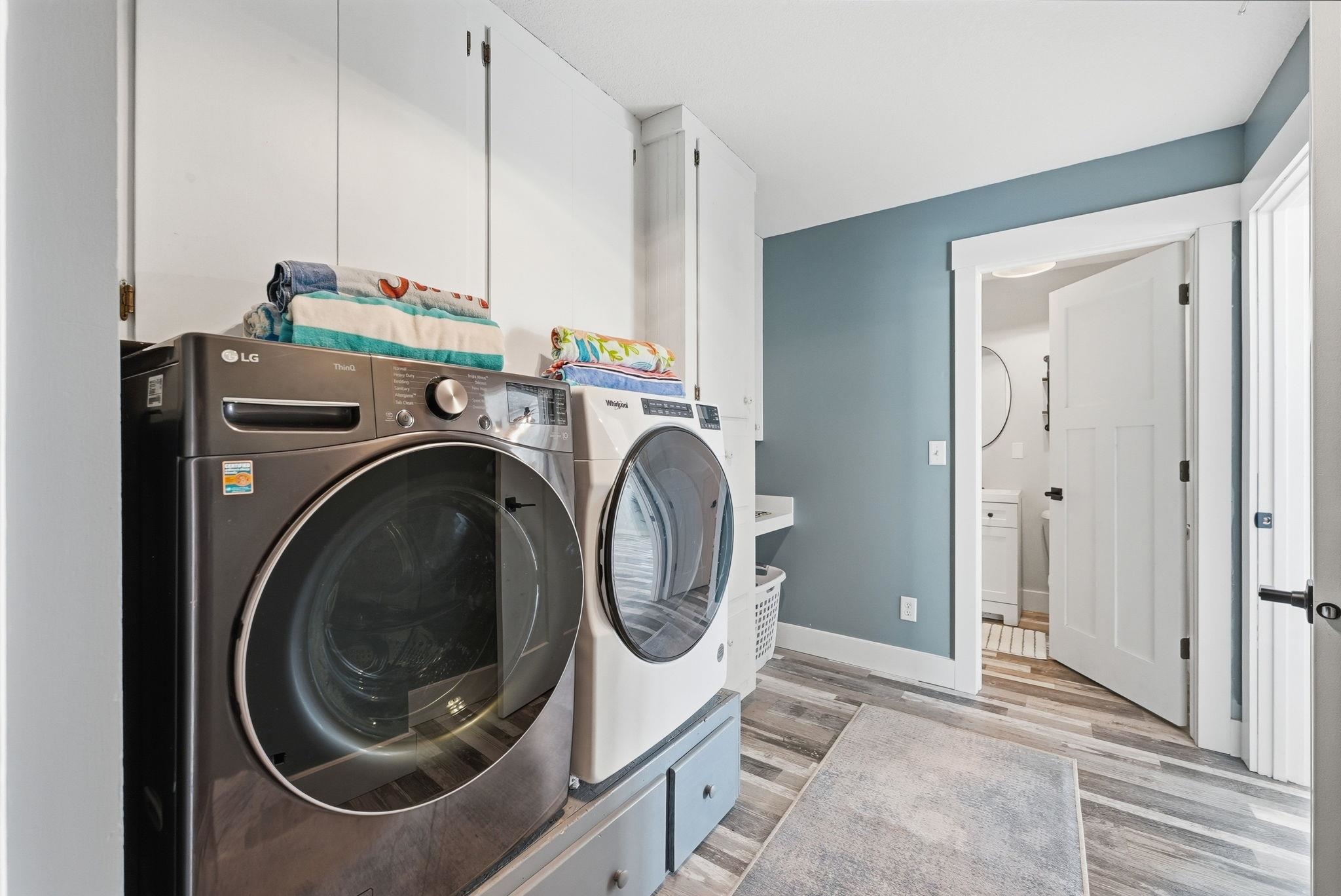 Dedicated laundry area featuring wood-finish flooring, white built-in cabinetry, and a painted accent wall
