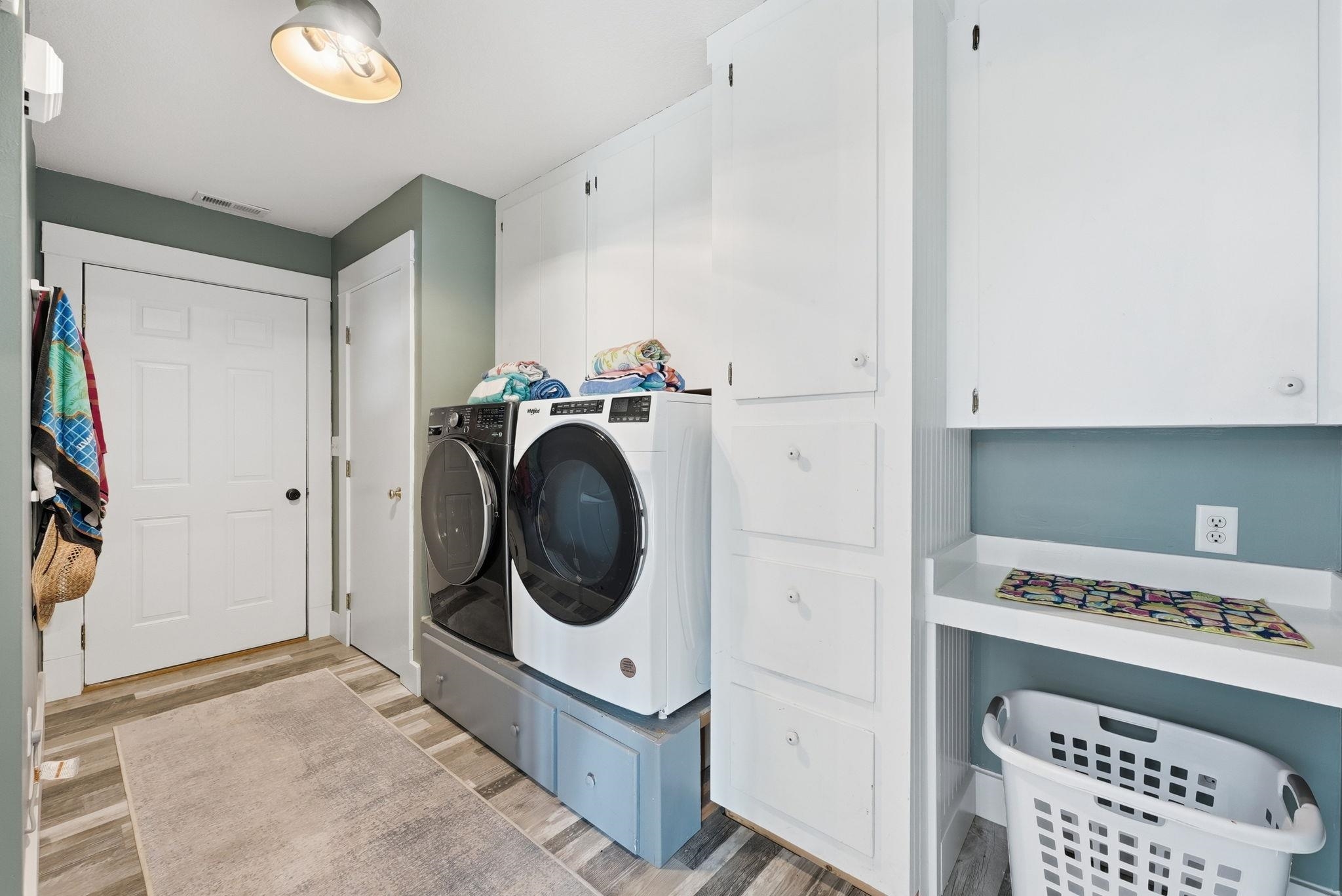 Dedicated laundry area featuring wood-finish flooring, extensive built-in white cabinetry, and a countertop workspace