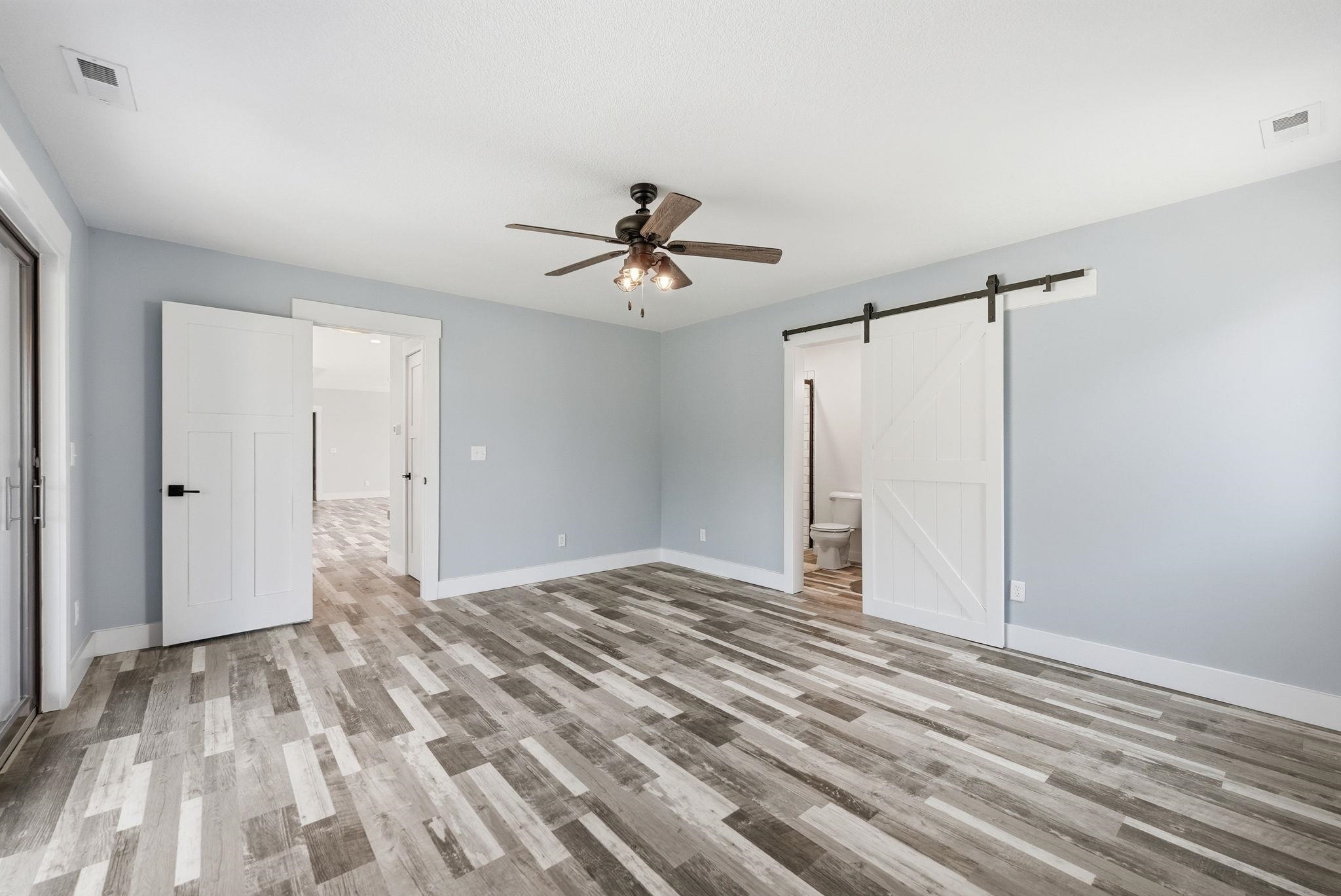 Spacious room featuring wood-finish flooring, a ceiling fan with integrated lighting, white baseboards, and light blue wall tones