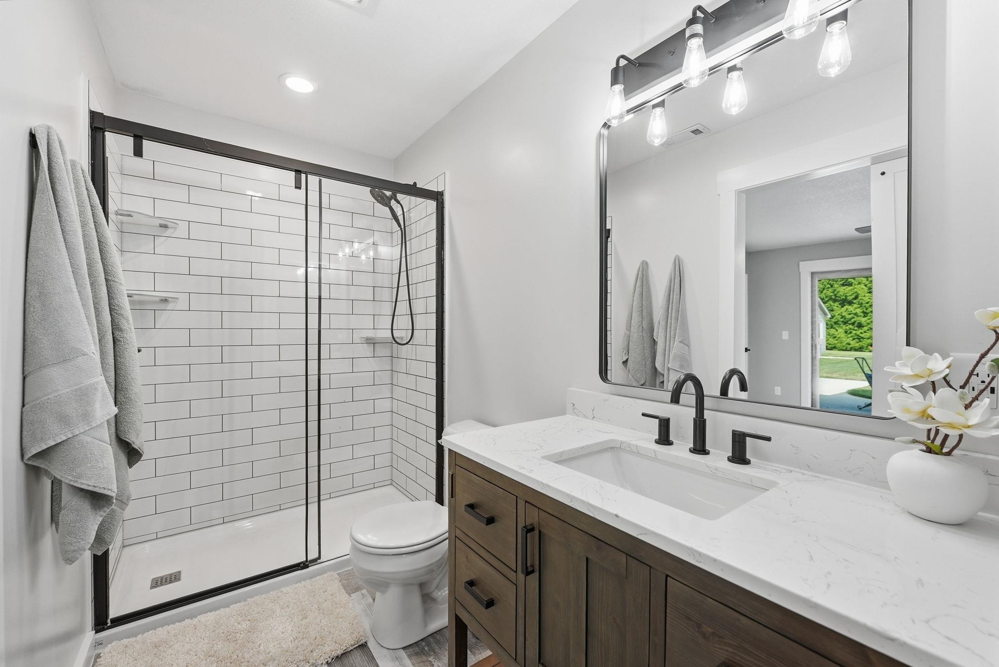 Bathroom featuring a dark wood-finish vanity with a white countertop and integrated sink, black-framed mirror, and a walk-in shower with subway tile surround and black-framed glass enclosure