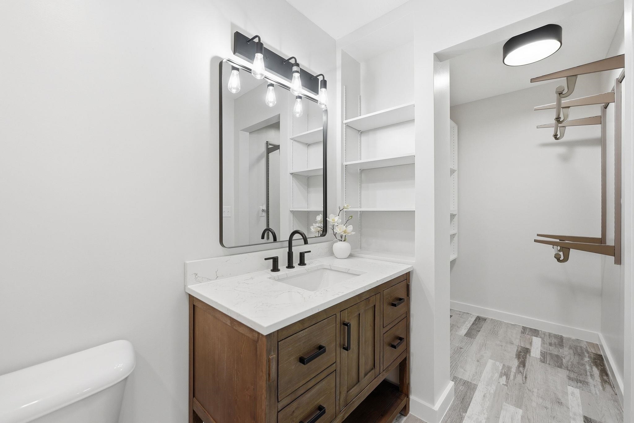 Bathroom featuring a wood-finish vanity with a white countertop and undermount sink, complemented by a rectangular mirror with a black frame and a three-light fixture