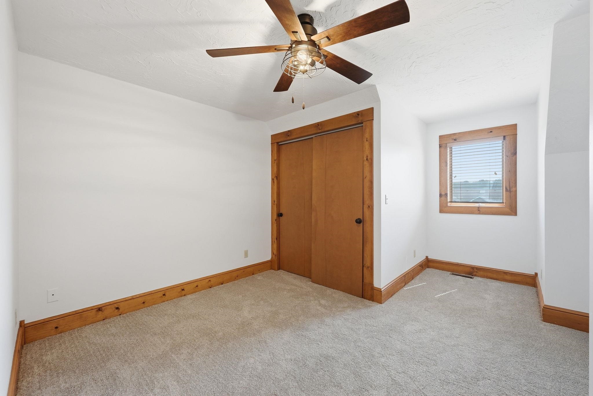 NEW Carpet featuring a new ceiling fan with industrial-style lighting, wood-trimmed window with blinds, wood bi-fold closet doors, and wood baseboards