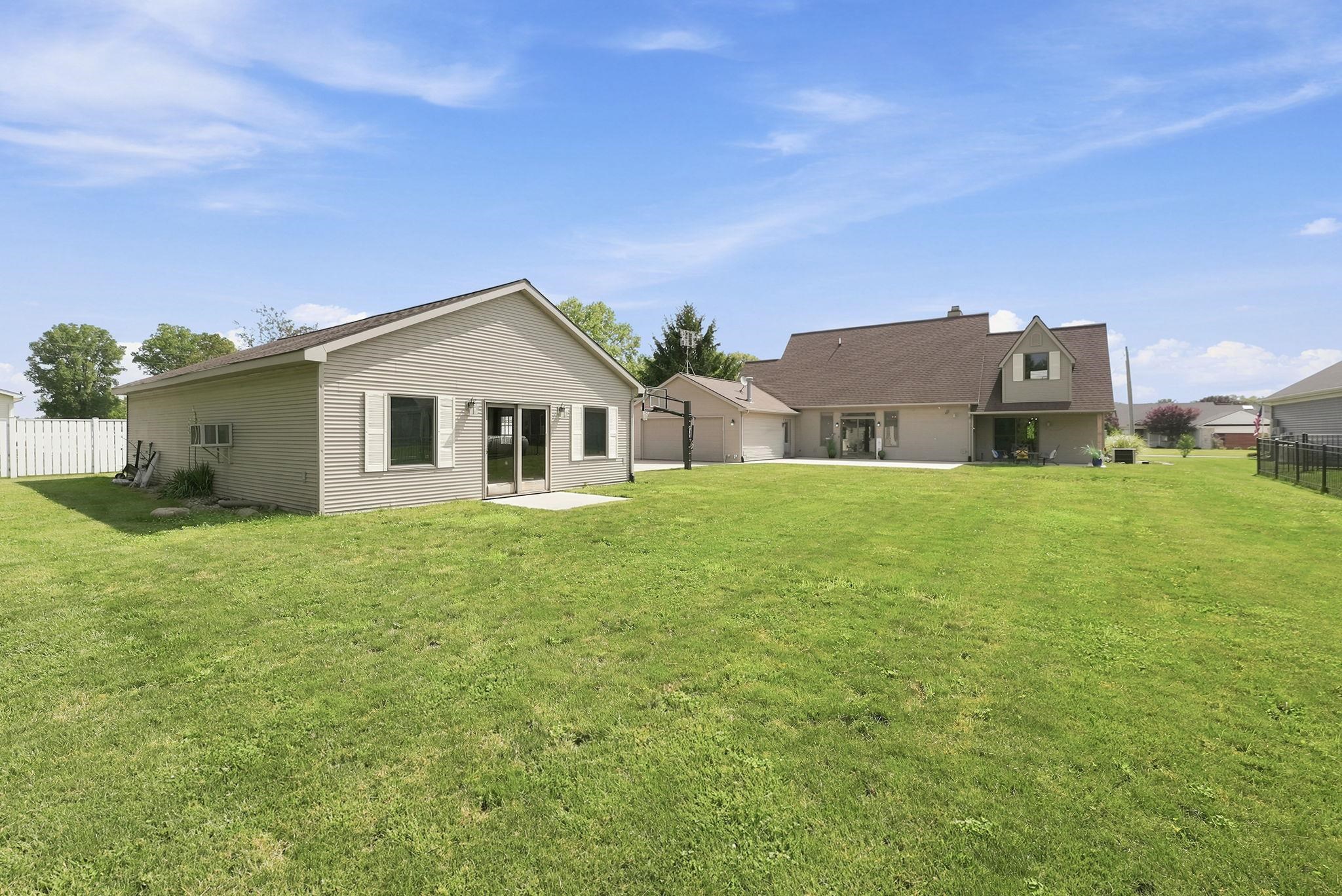 Expansive green lawn with a detached auxiliary building featuring light-colored siding, multiple windows with shutters, and a set of glass patio doors