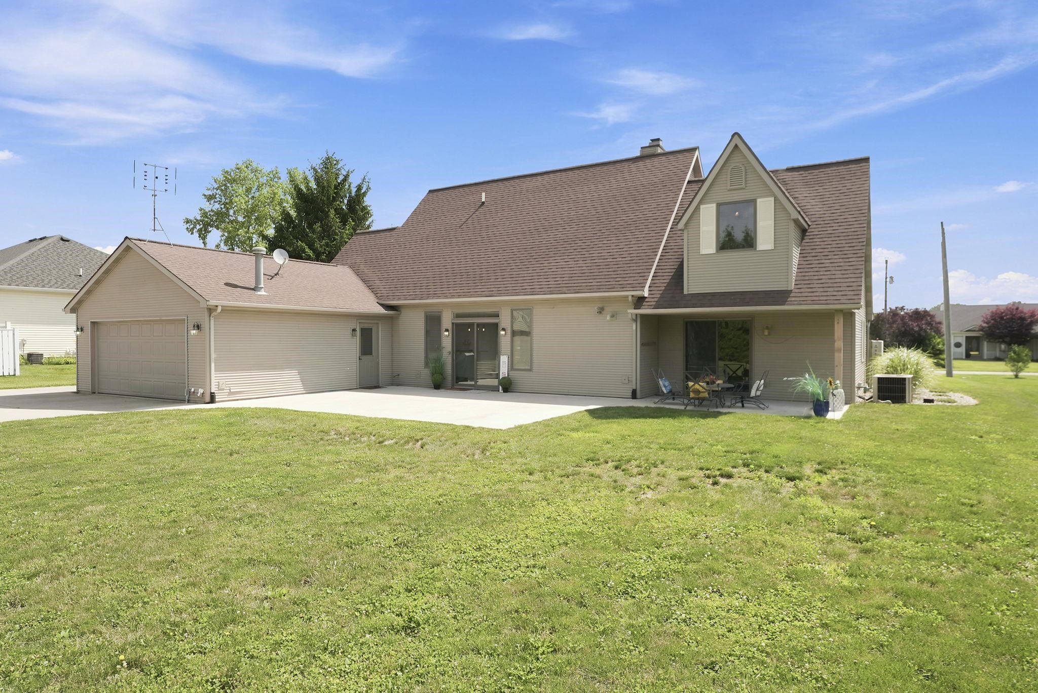 Ranch-style residence featuring a two-car attached garage, a dormer window, a concrete patio, and a shingle roof
