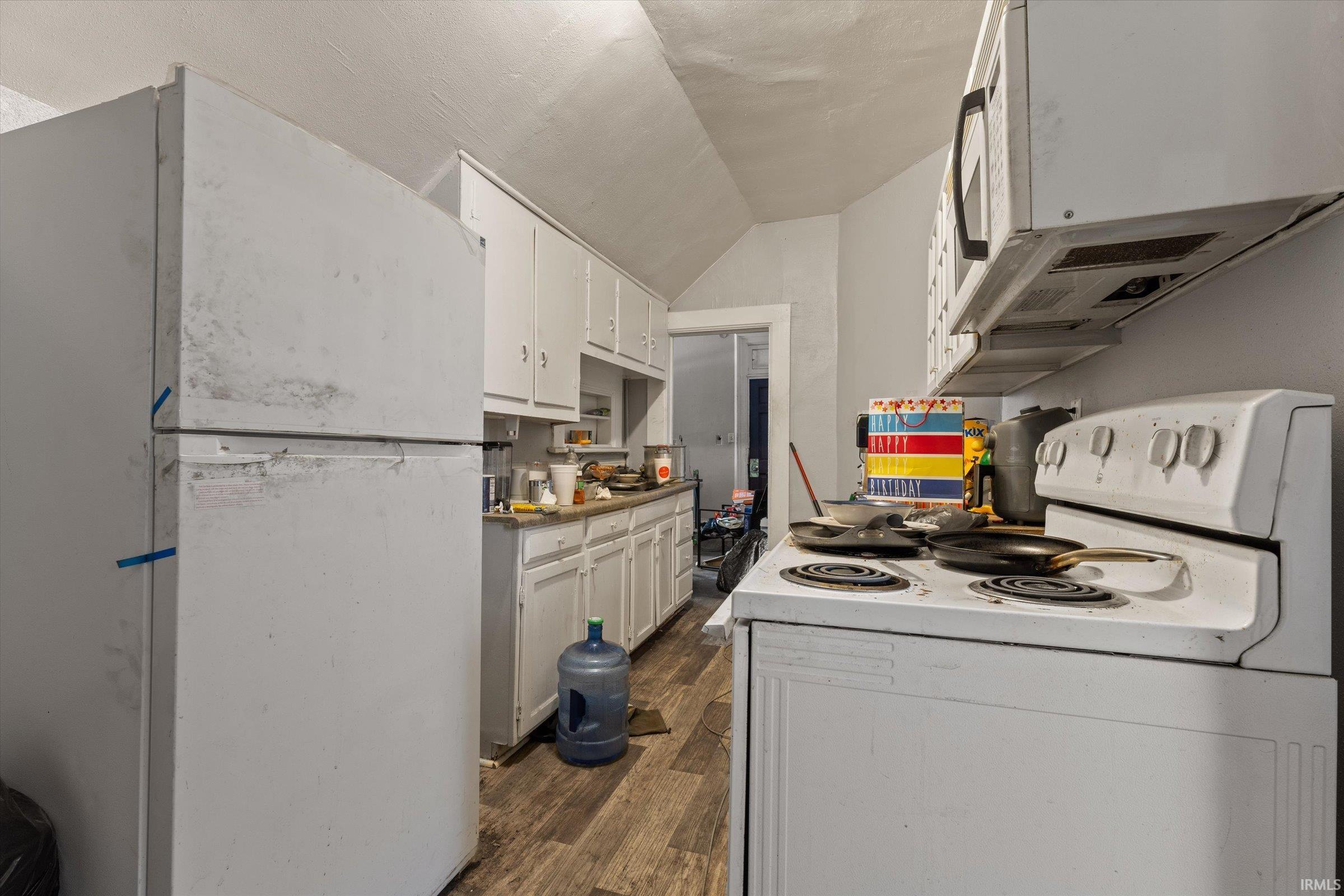 Kitchen with white appliances, white cabinets, dark wood-type flooring, and light countertops