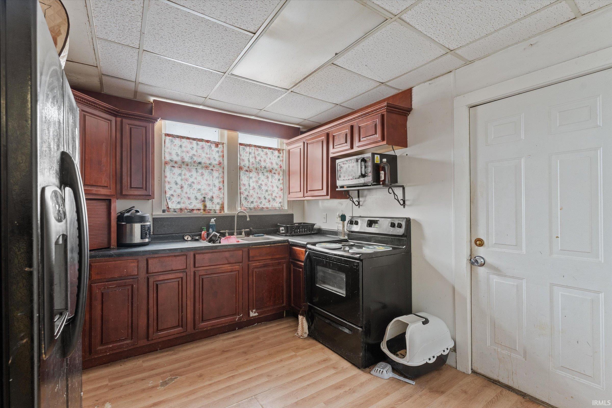 Kitchen featuring black appliances, dark countertops, light wood-style flooring, and a paneled ceiling