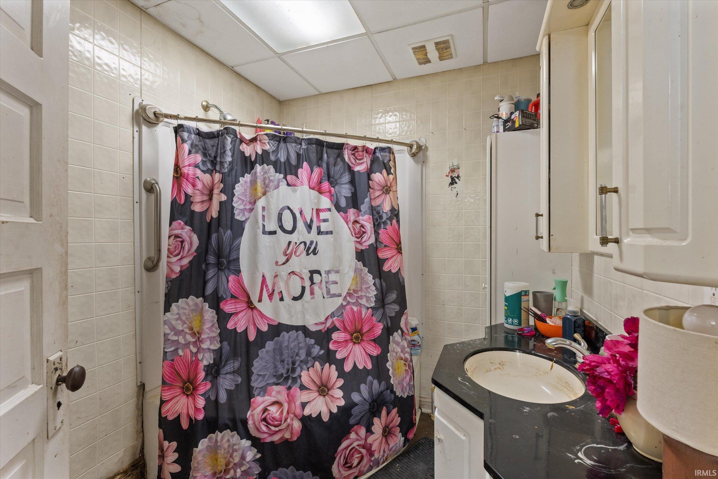 Bathroom with tile walls, vanity, shower / bath combo with shower curtain, and a drop ceiling