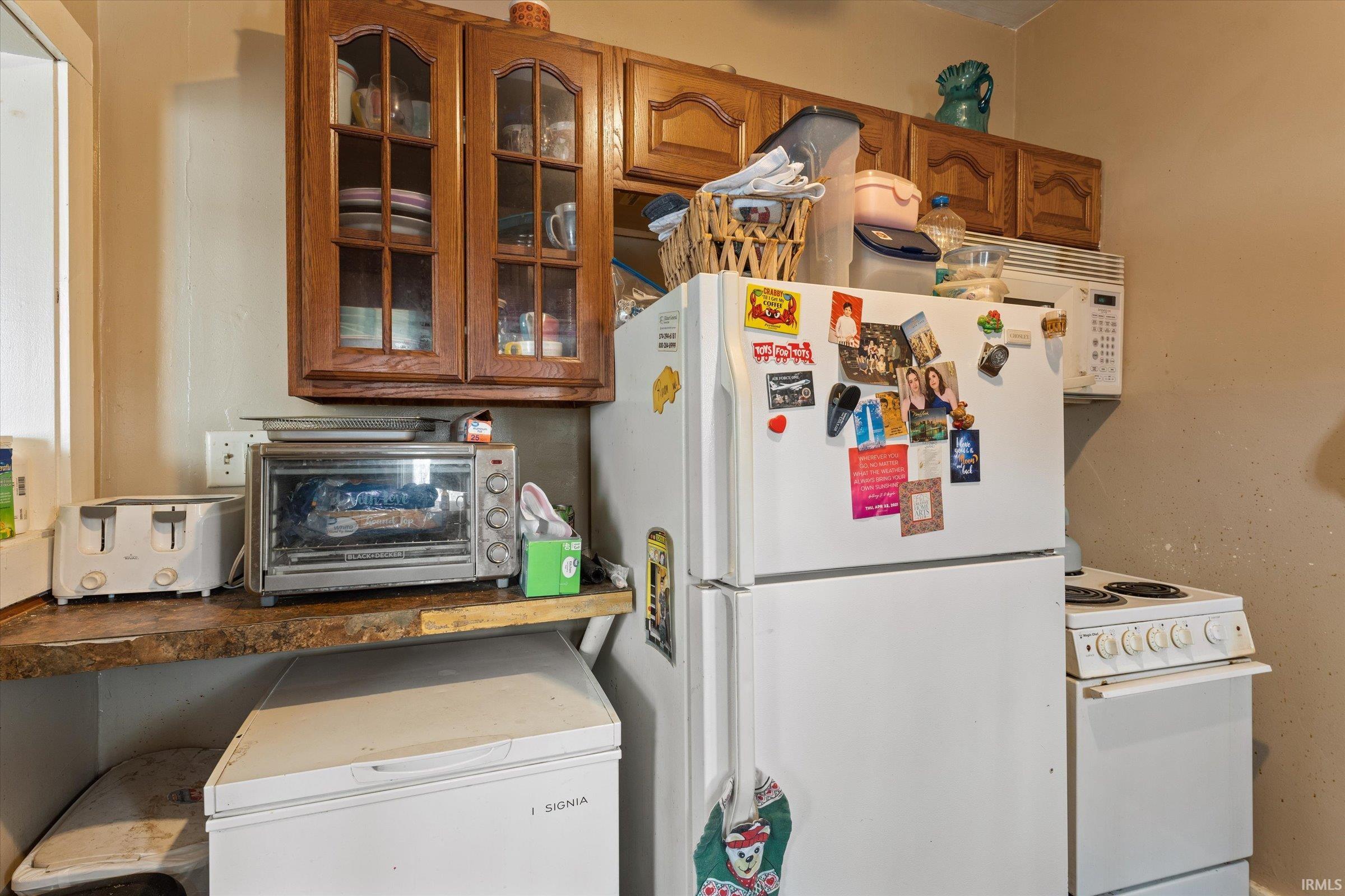 Kitchen with white appliances, glass insert cabinets, wood finish cabinetry, and dark countertops