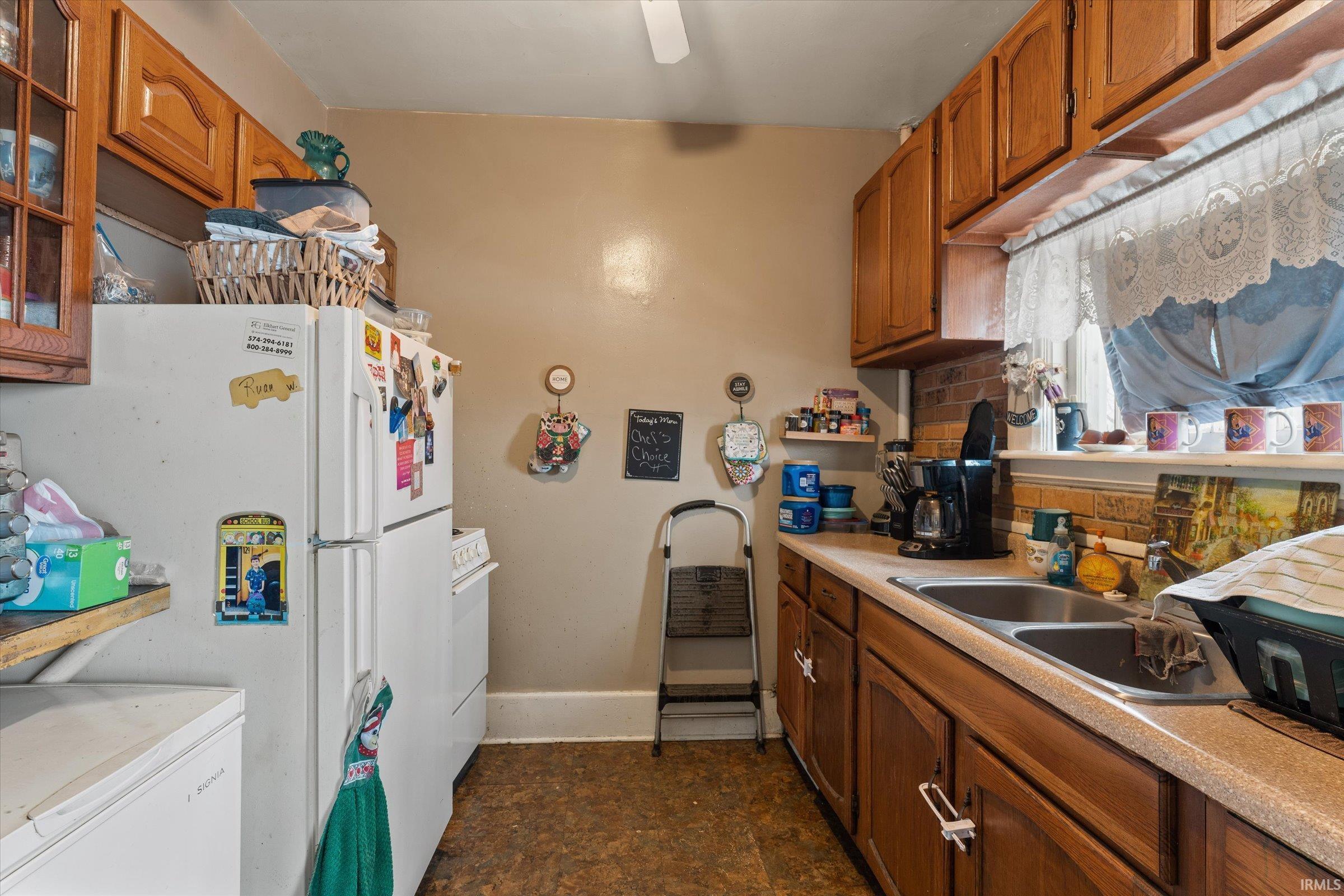 Kitchen with wood finish cabinets, light countertops, white appliances, and decorative backsplash